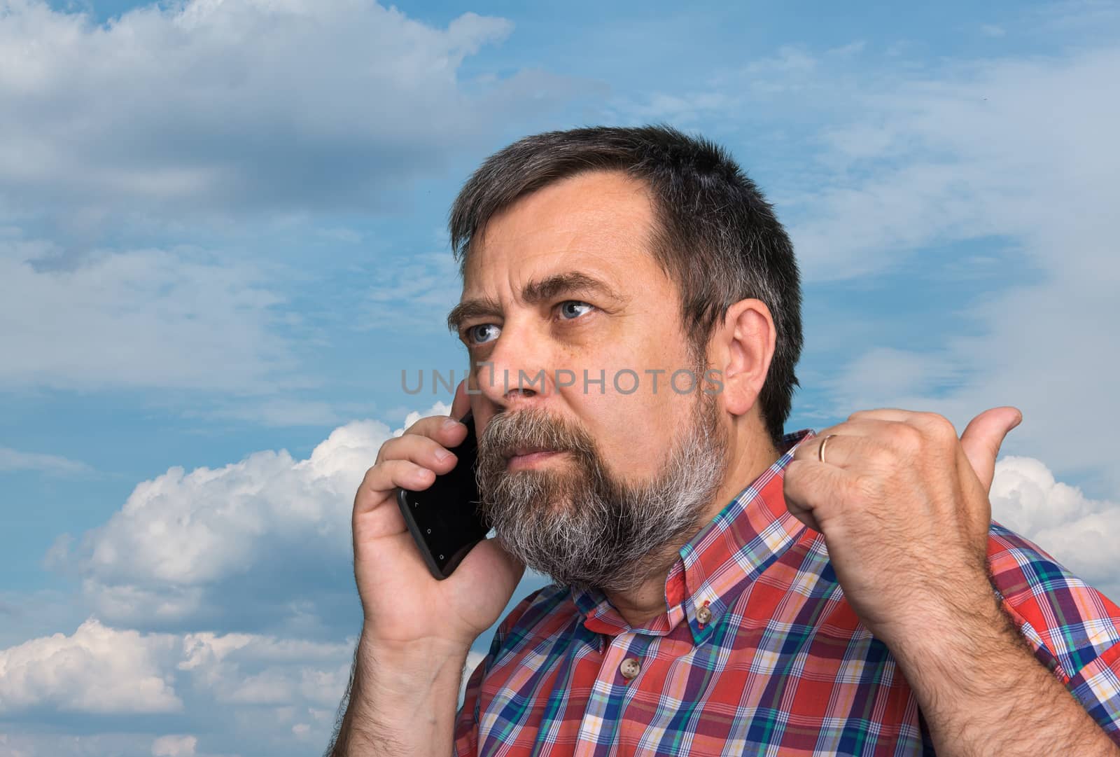 Middle-aged man speaks on a mobile phone and raised thumb up showing sign ok against the sky with clouds