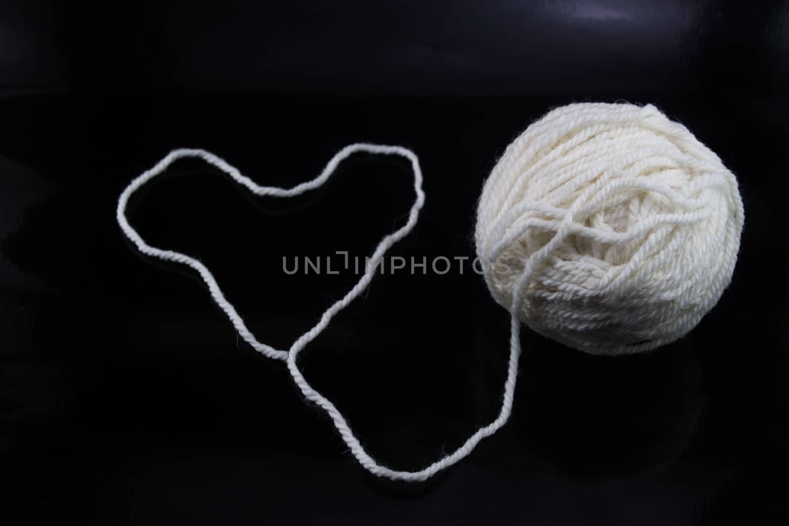 The white ball of wool thread on a black background, with the thread