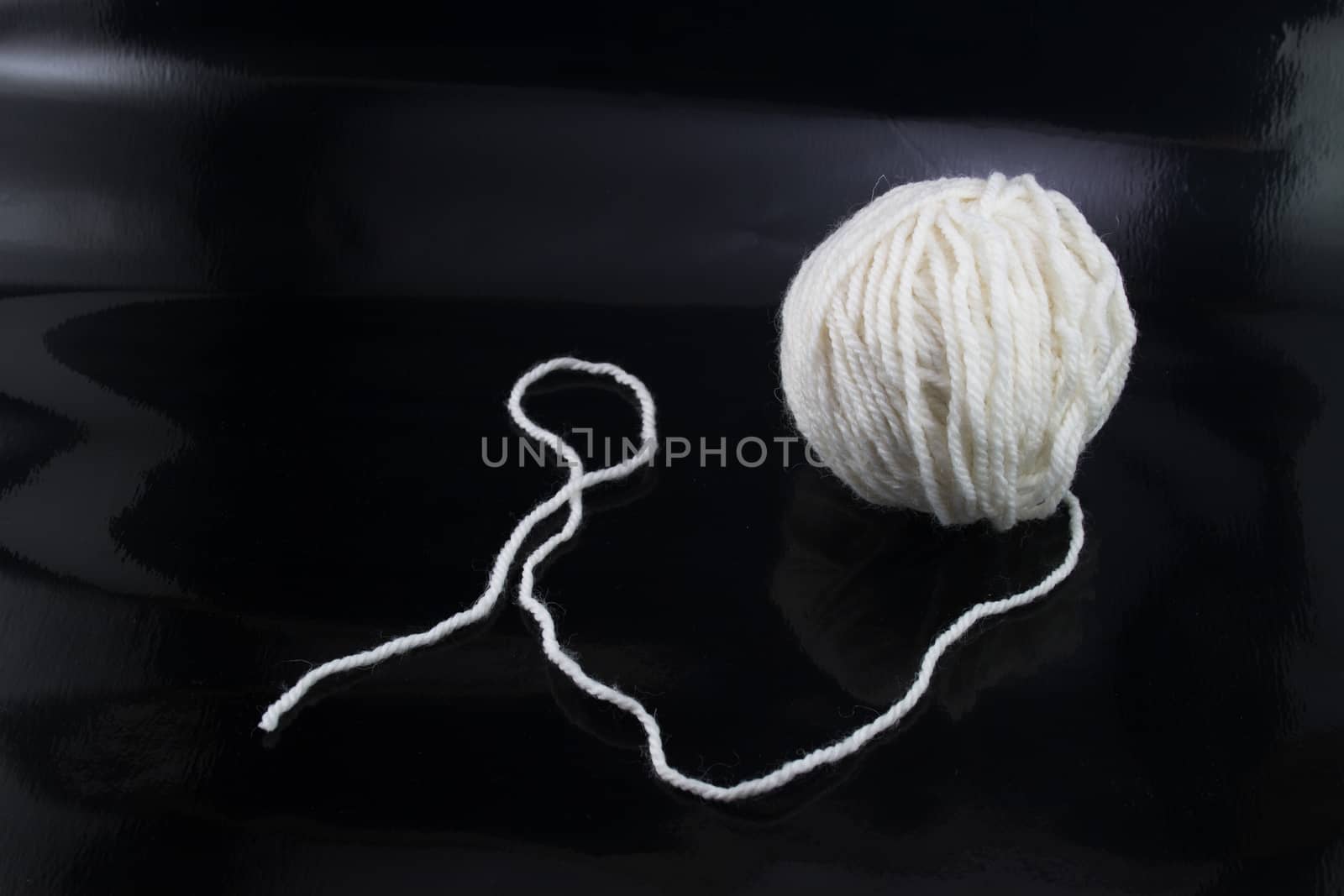 The white ball of wool thread on a black background, with the thread