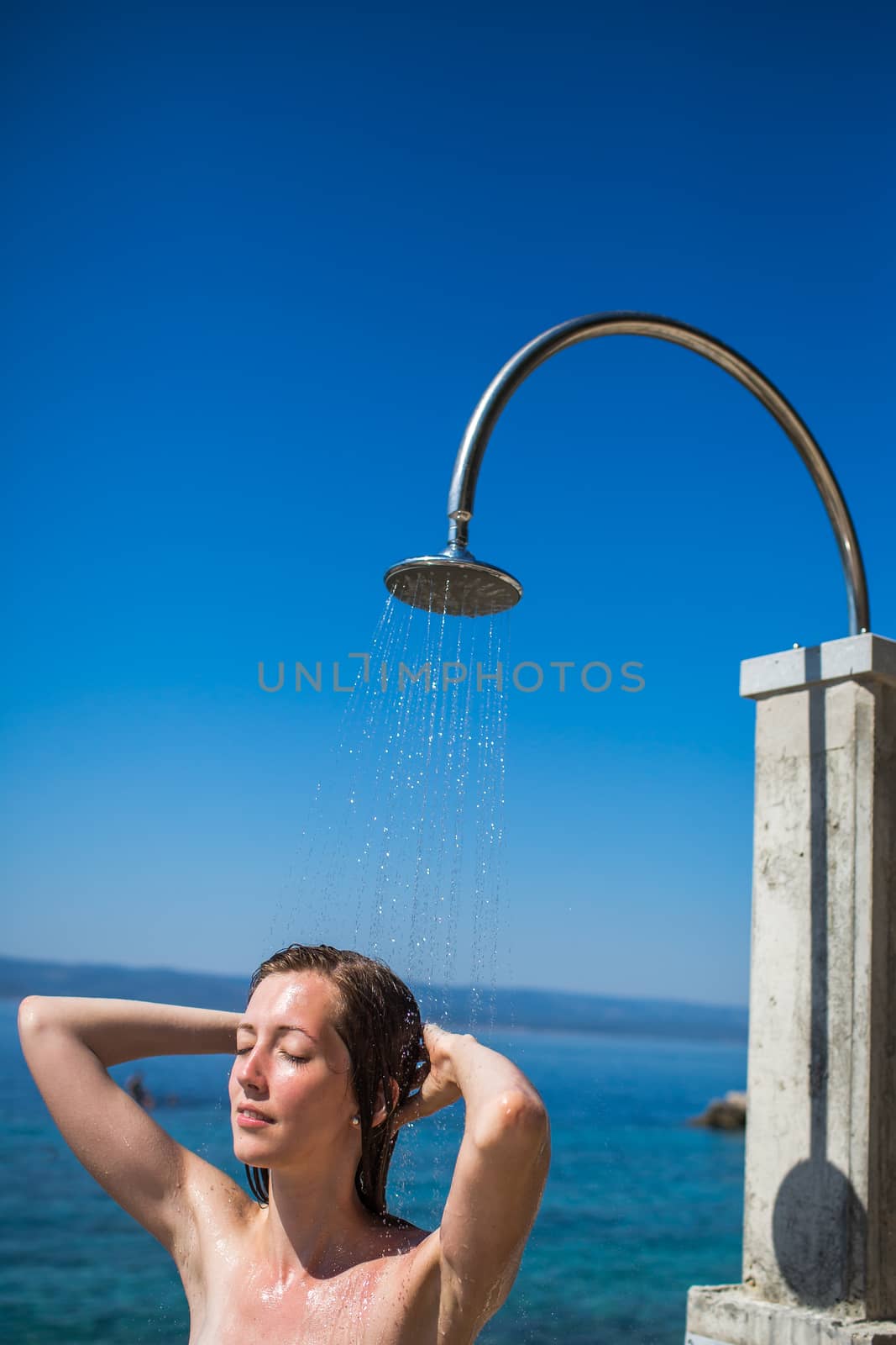 Pretty, young woman woman under shower on the beach after swimming