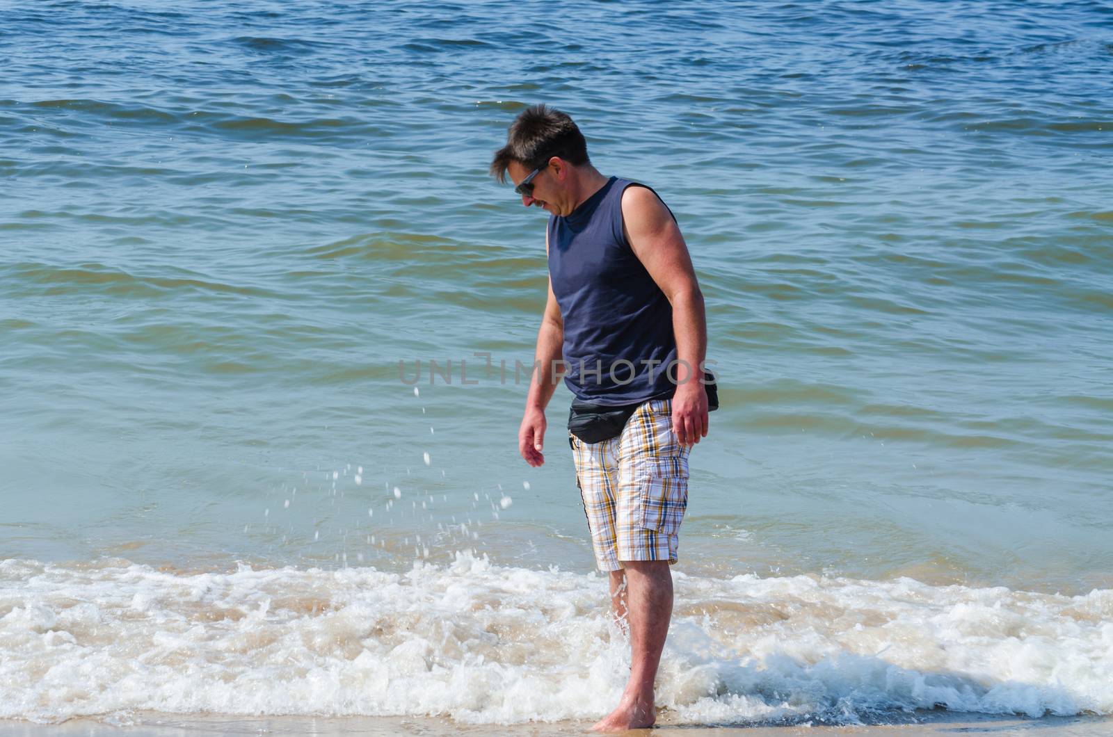 Man in shorts, T-shirt and sun glasses at the beach with your feet in the water.