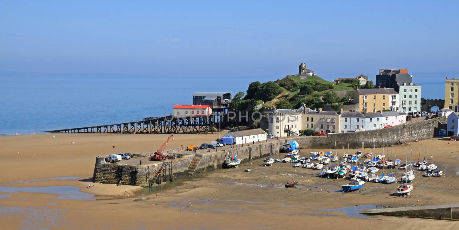 A view of Tenby harbour, in south Wales, with colourful, pastel houses overlooking the beach and sea, with the tide out