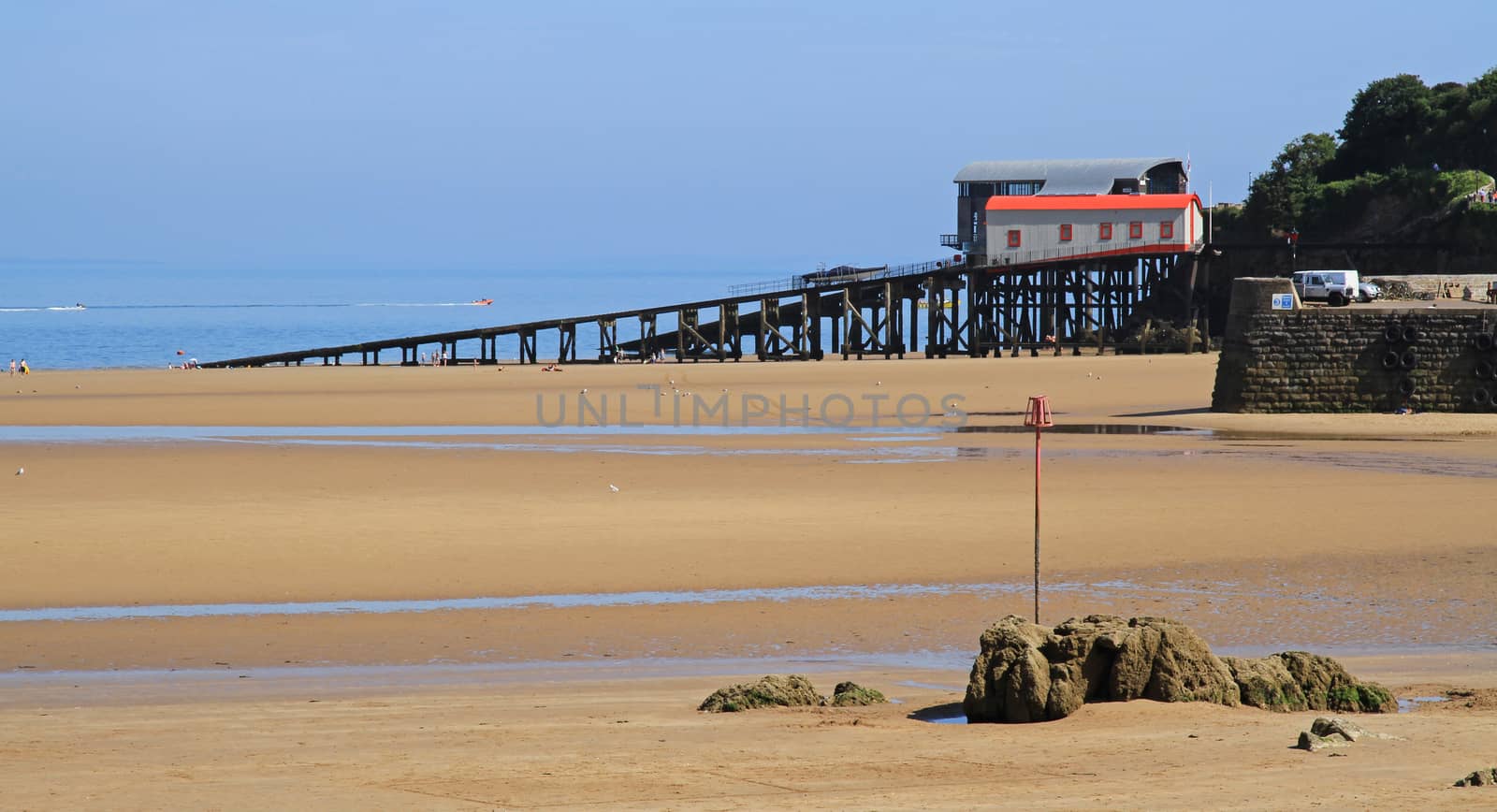A wide beach, on a summers day, with a lifeboat station slip, leading into the sea, in Tenby