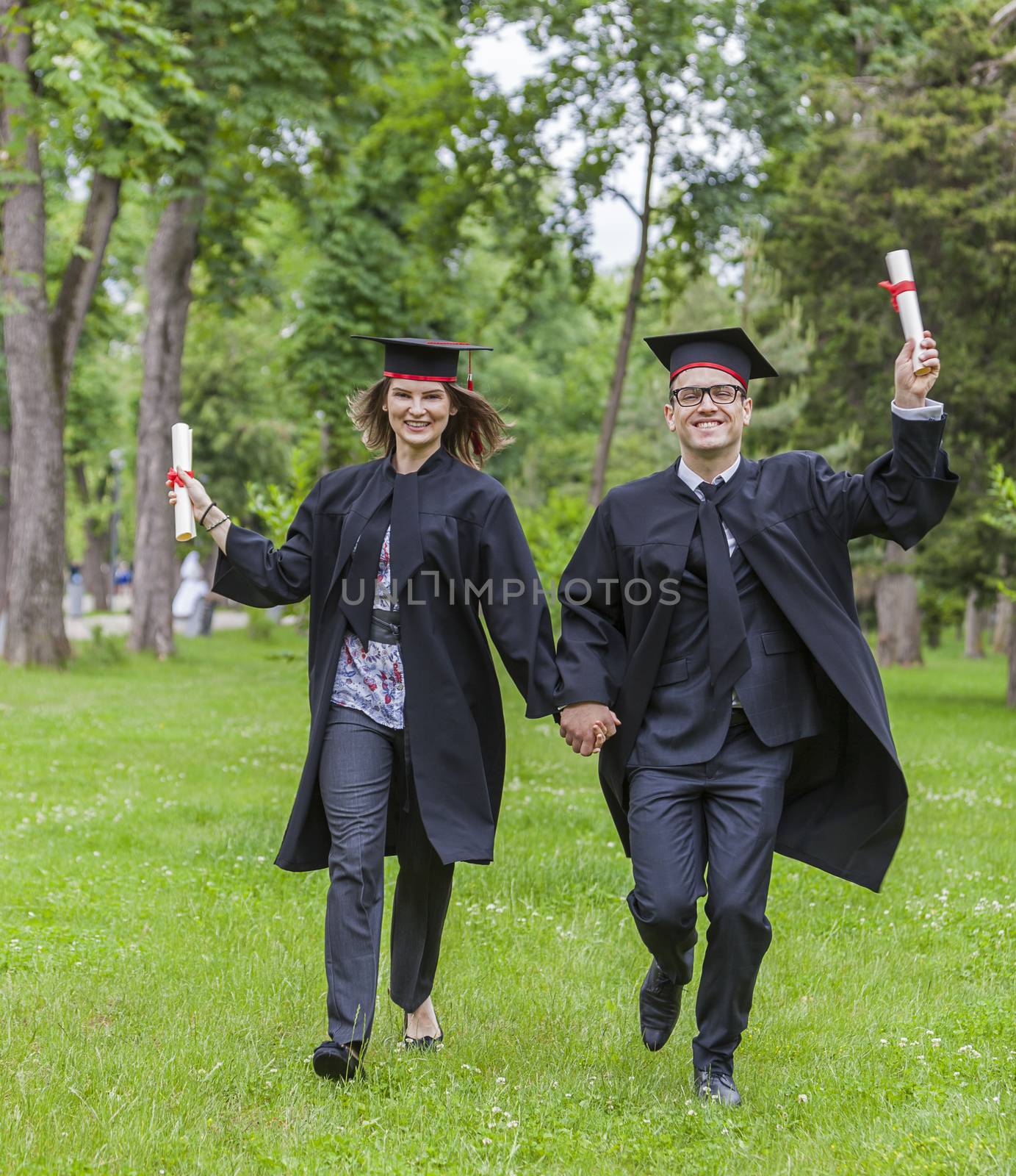 Young happy couple running in a green park in the graduation day.