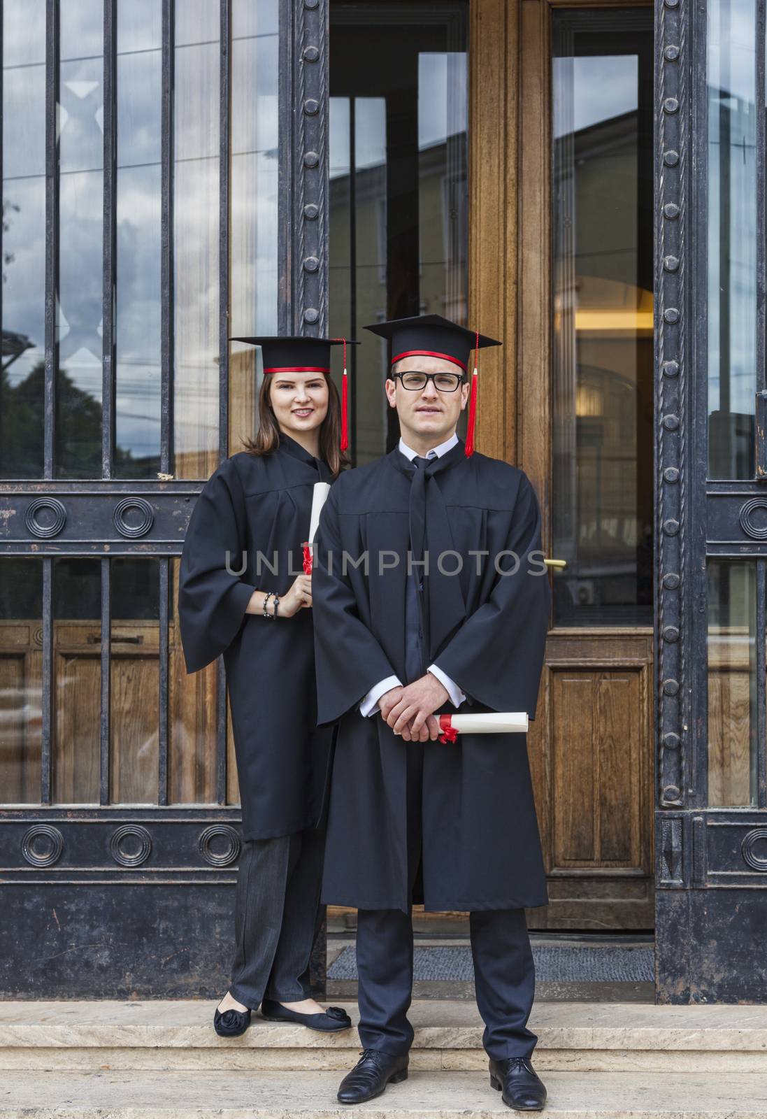 Young couple in the graduation day posing in front of the gate of the University.