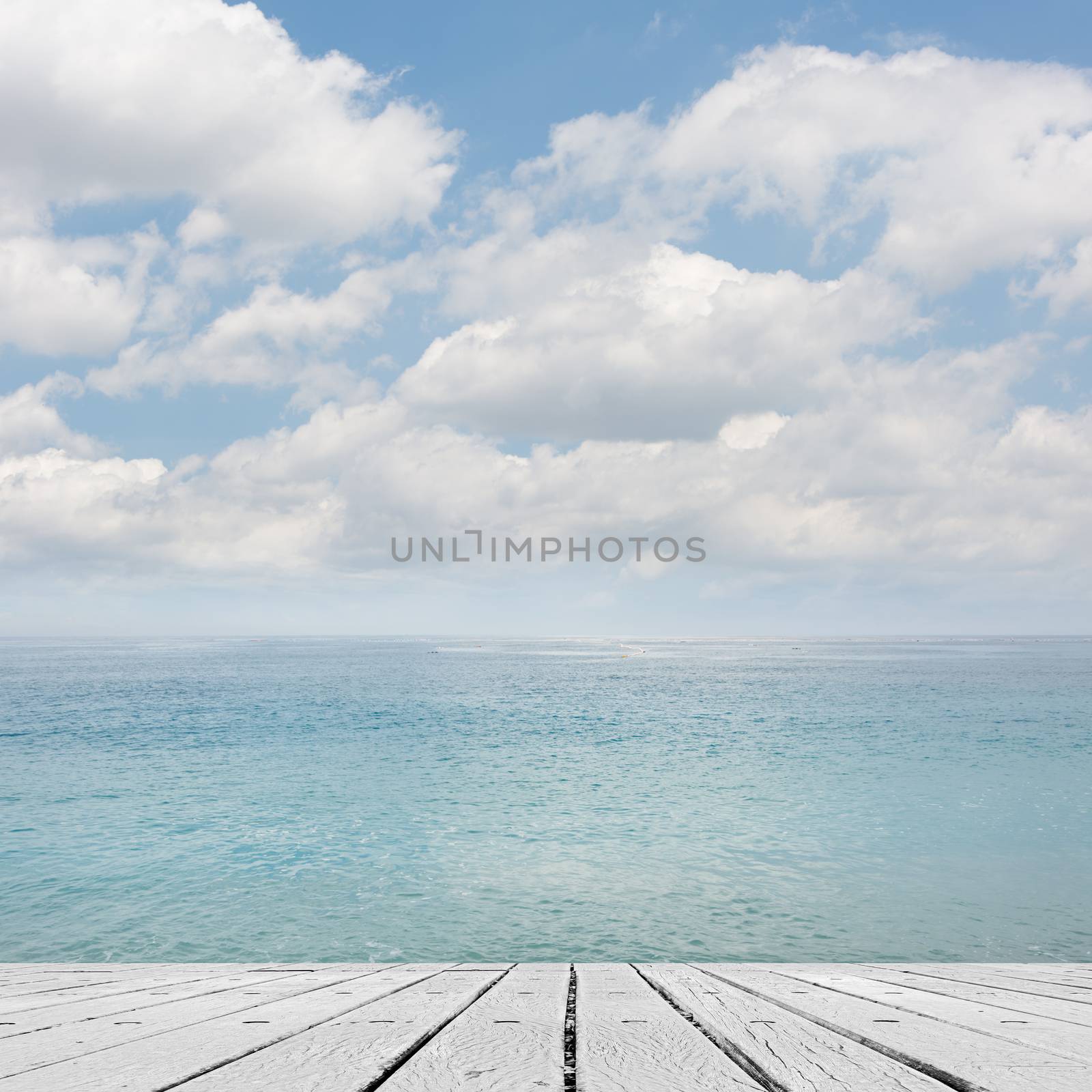 Empty wooden deck table with copyspace under sunny cloudy sky in the beach, focus on the wooden ground.