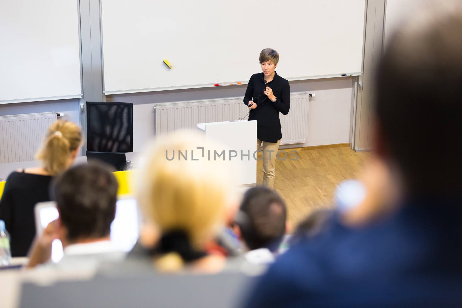 Speaker giving presentation in lecture hall at university. Participants listening to lecture and making notes.