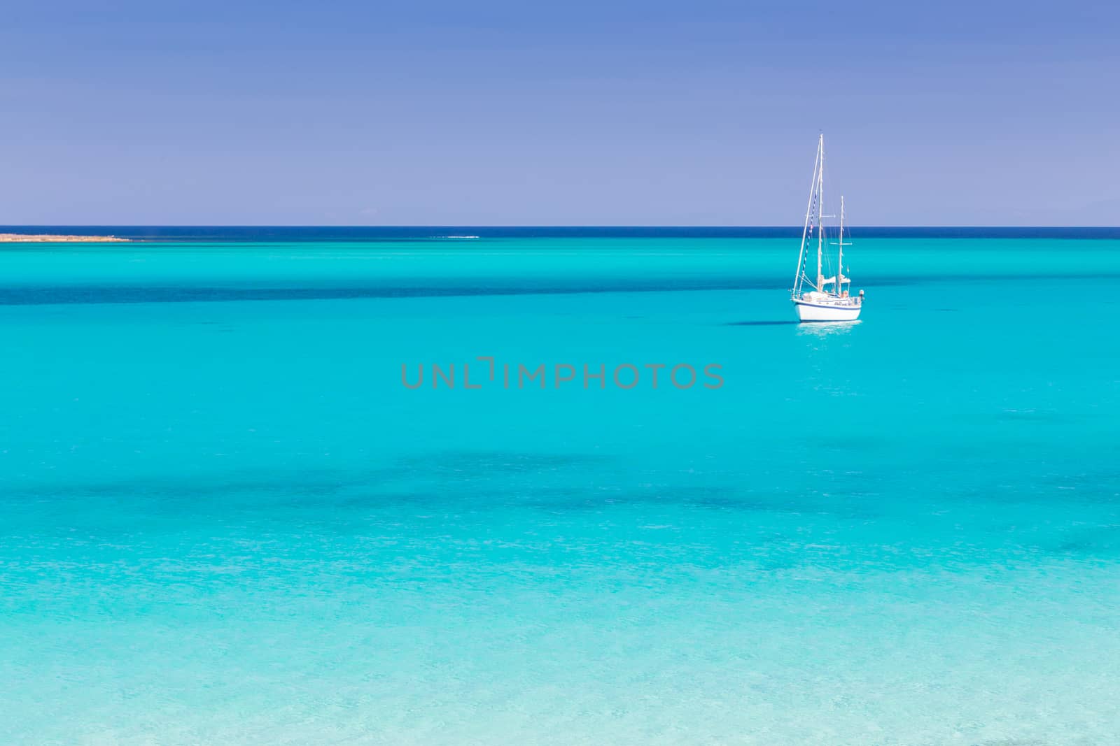 White sail boat at the beautiful turquoise blue mediterranean Pelosa beach near Stintino,Sardinia, Italy.