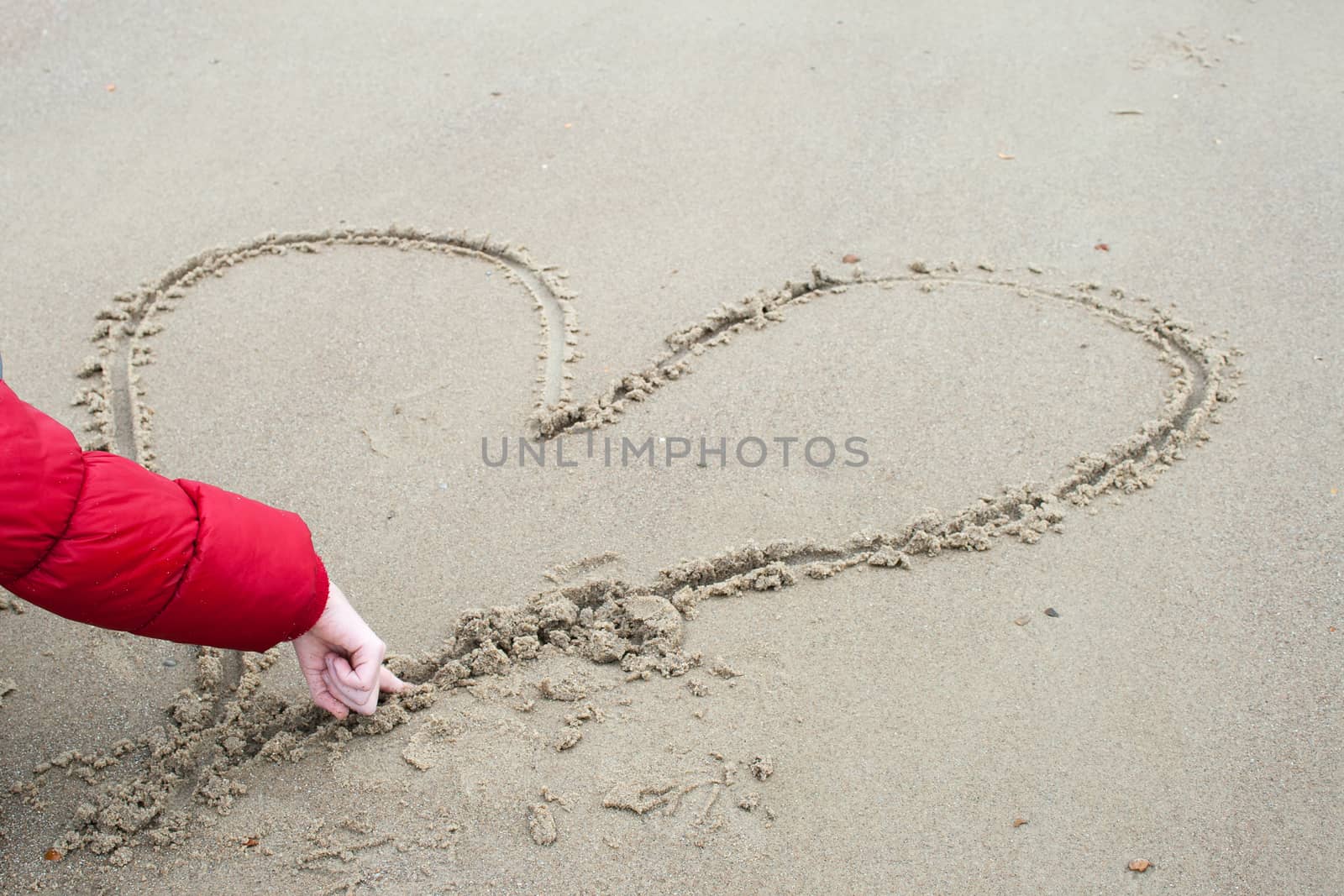 child is drawing in the sand  a heart by Havana