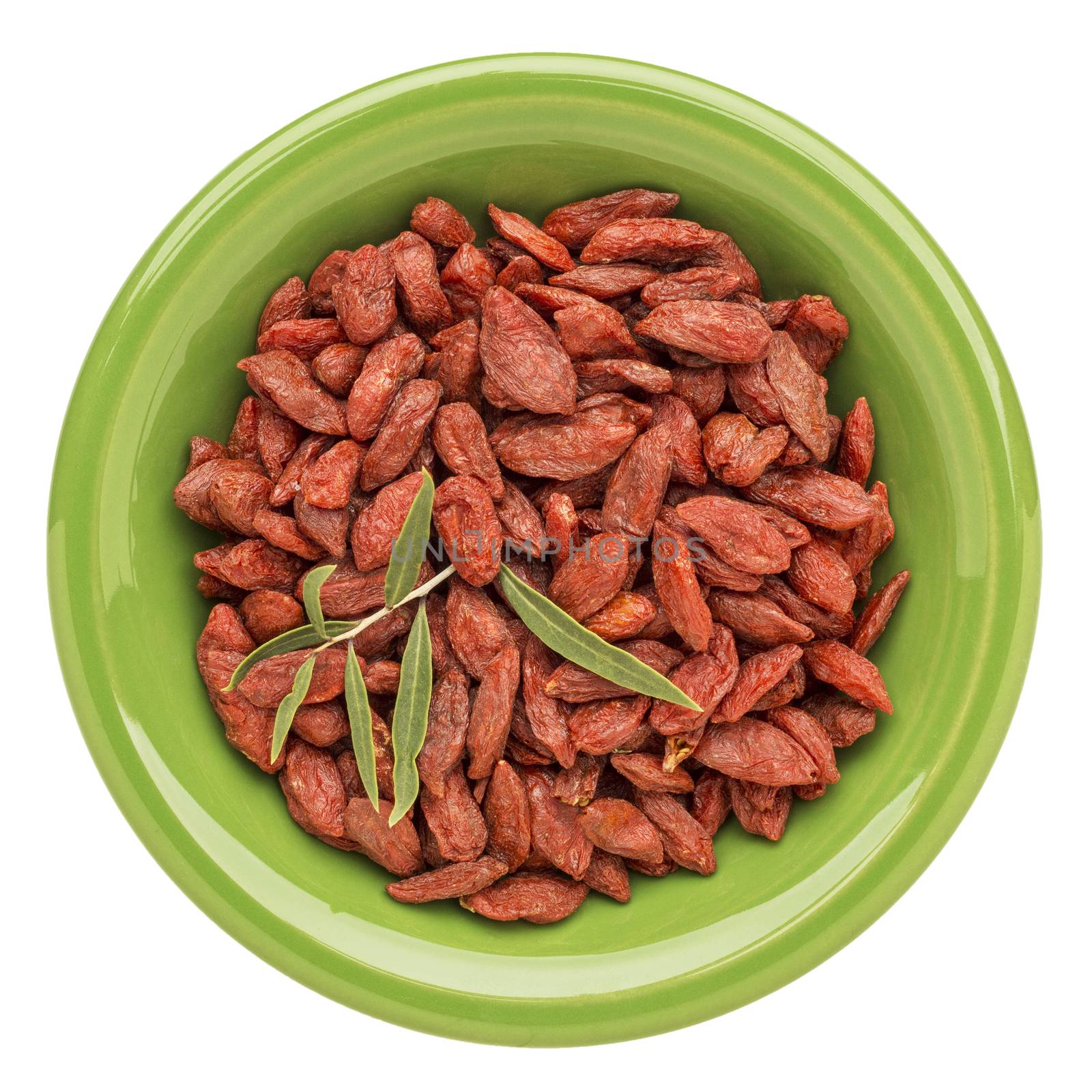 dried goji berries with a fresh leaf on an isolated green ceramic bowl