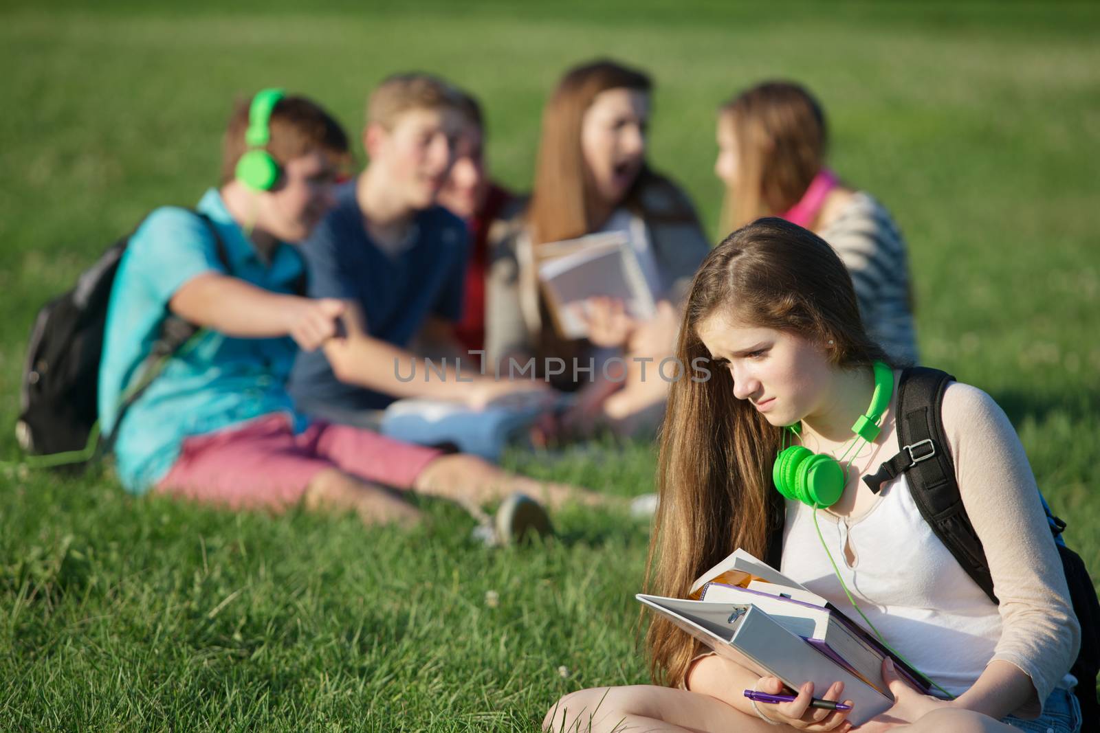 Sad female teenager sitting outdoors with books