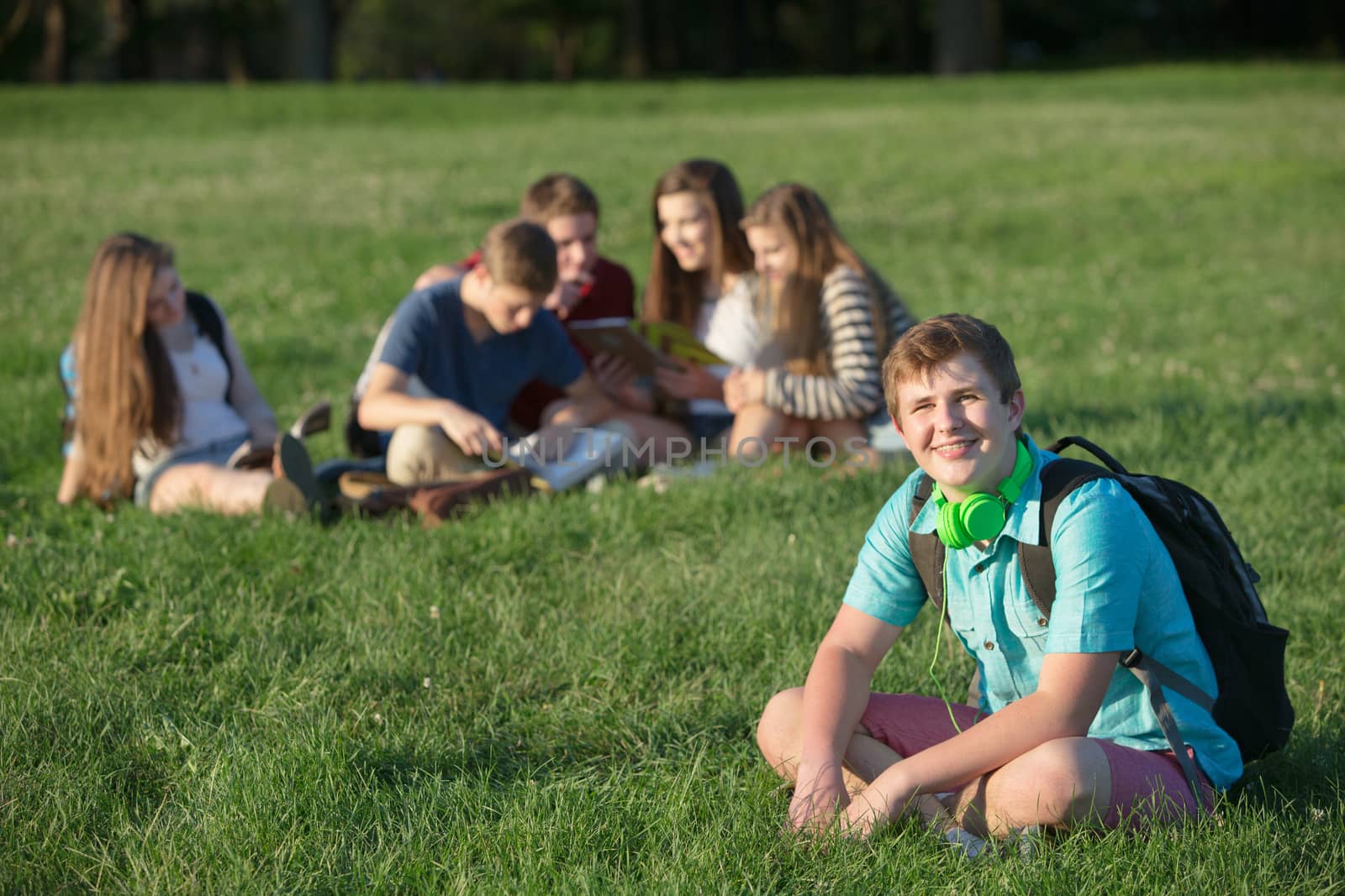 Handsome European teen male student sitting on lawn