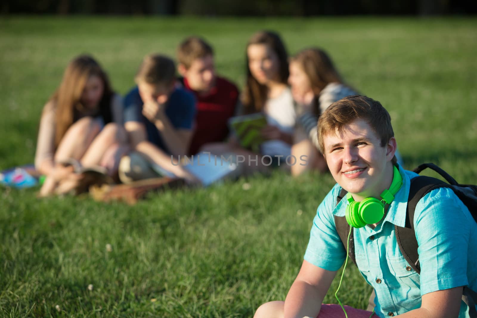Smiling teen student with earphones sitting outdoors