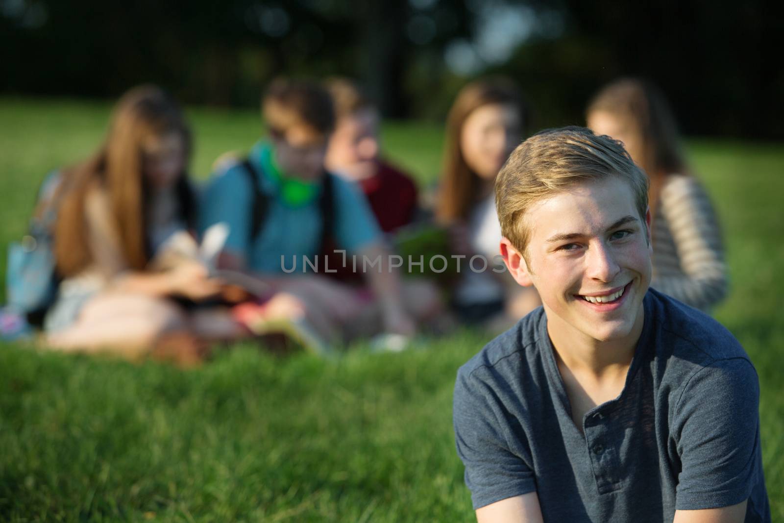 Happy Caucasian male teenager sitting near group