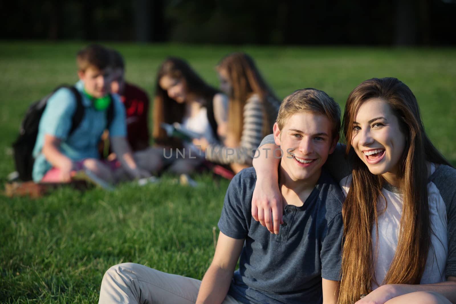 Happy teen girlfriend and boyfriend sitting outdoors