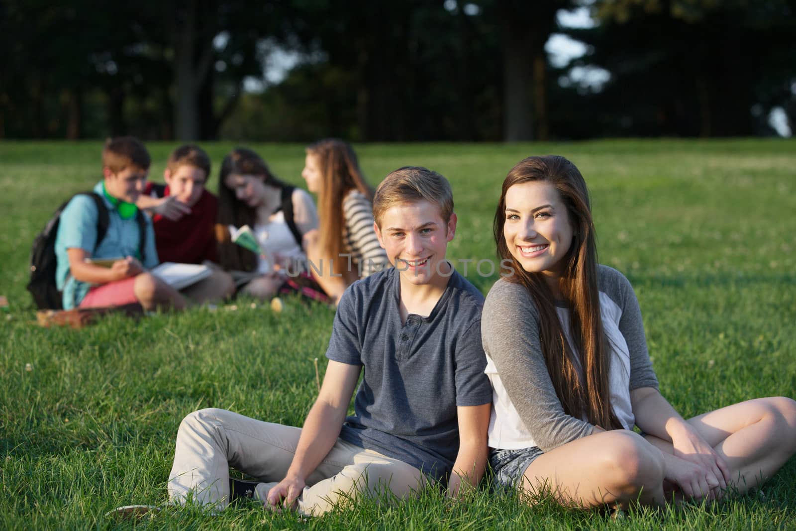 Two happy teenage male and female friends sitting outdoors