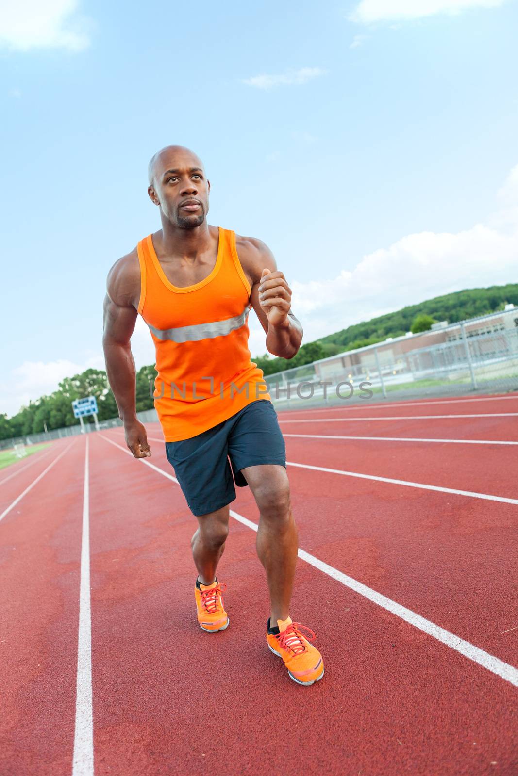 African American man in his 30s running at a sports track outdoors.