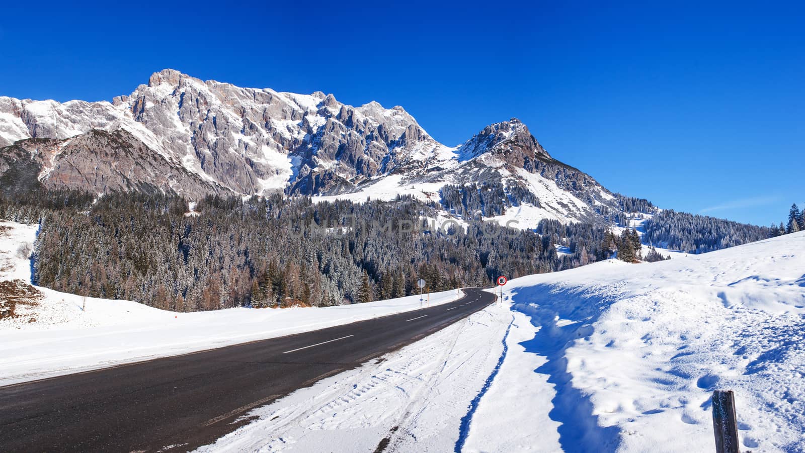 Panorama of winter in the Austrian alps mountain. Asphalt road among snow.