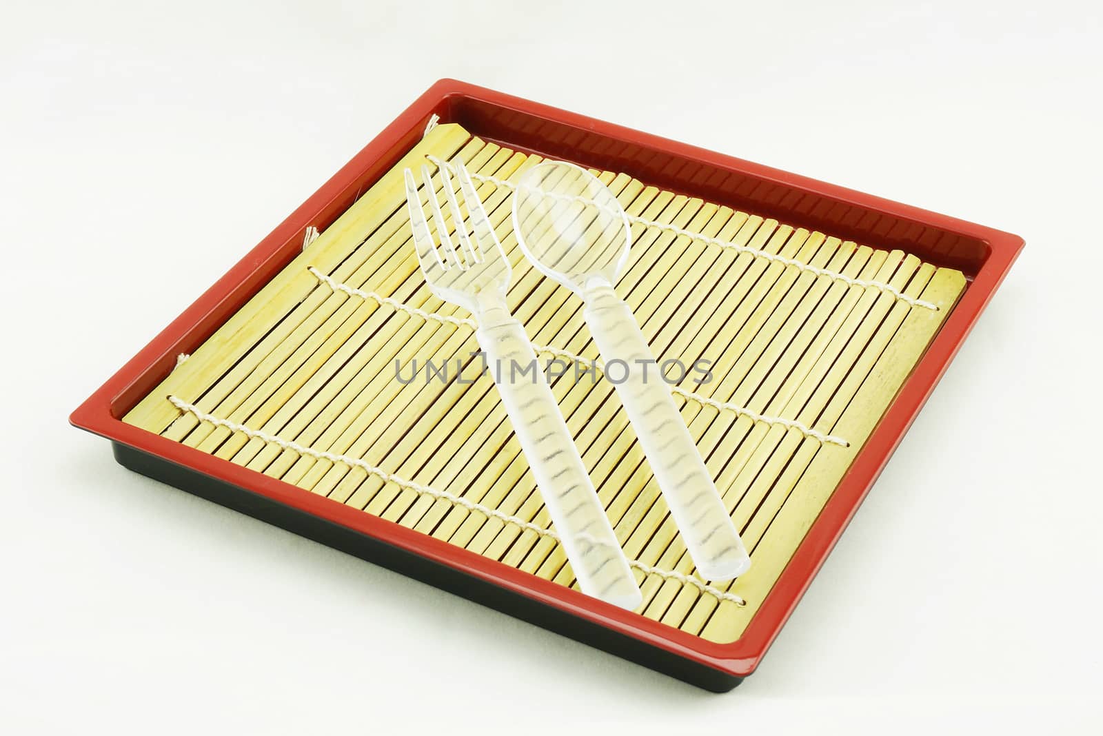 Spoon and fork are white color, placed on bamboo pad in wooden tray.                                