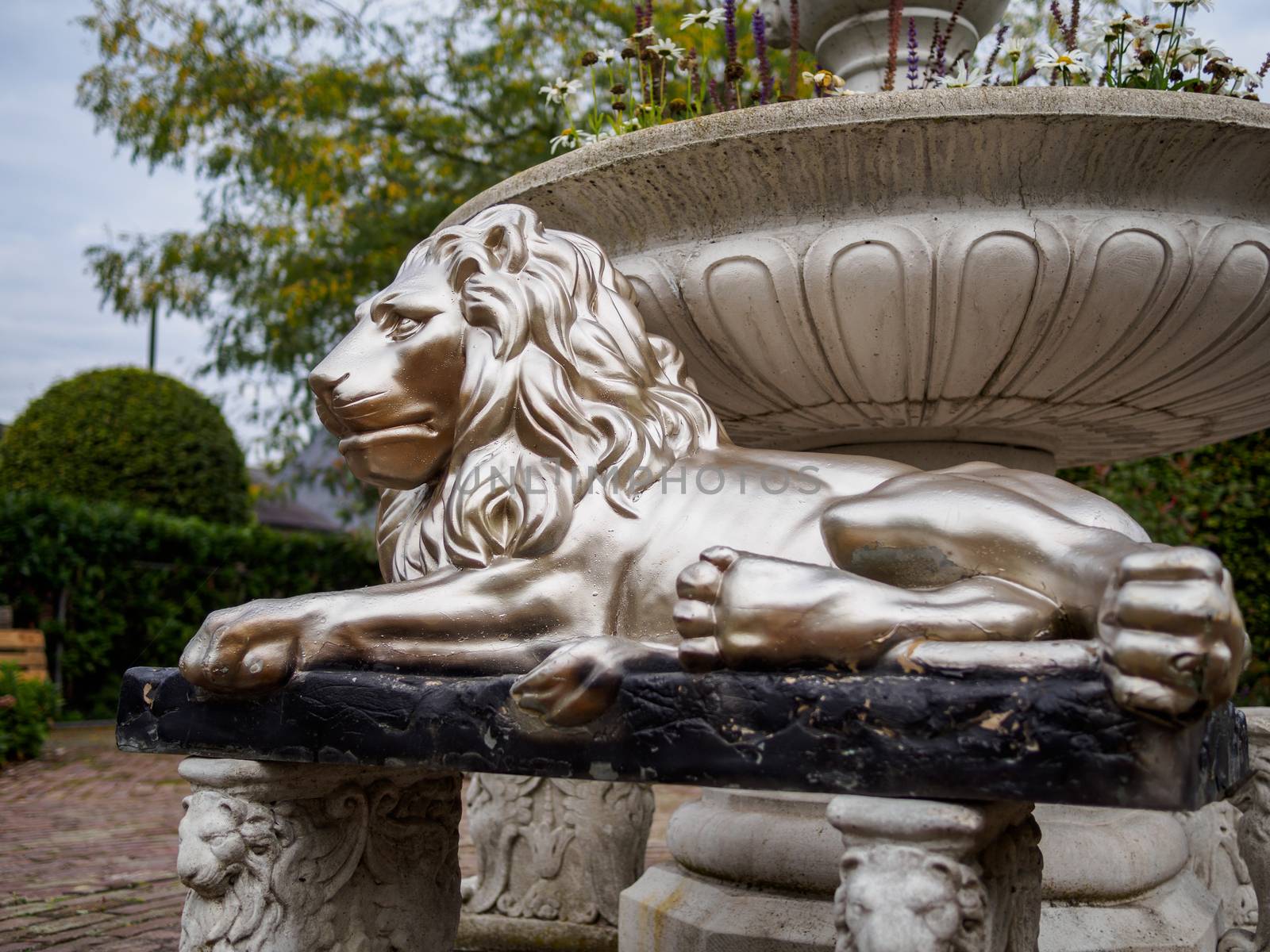 Lying proud under a stone fountain is this large silver lyon statue