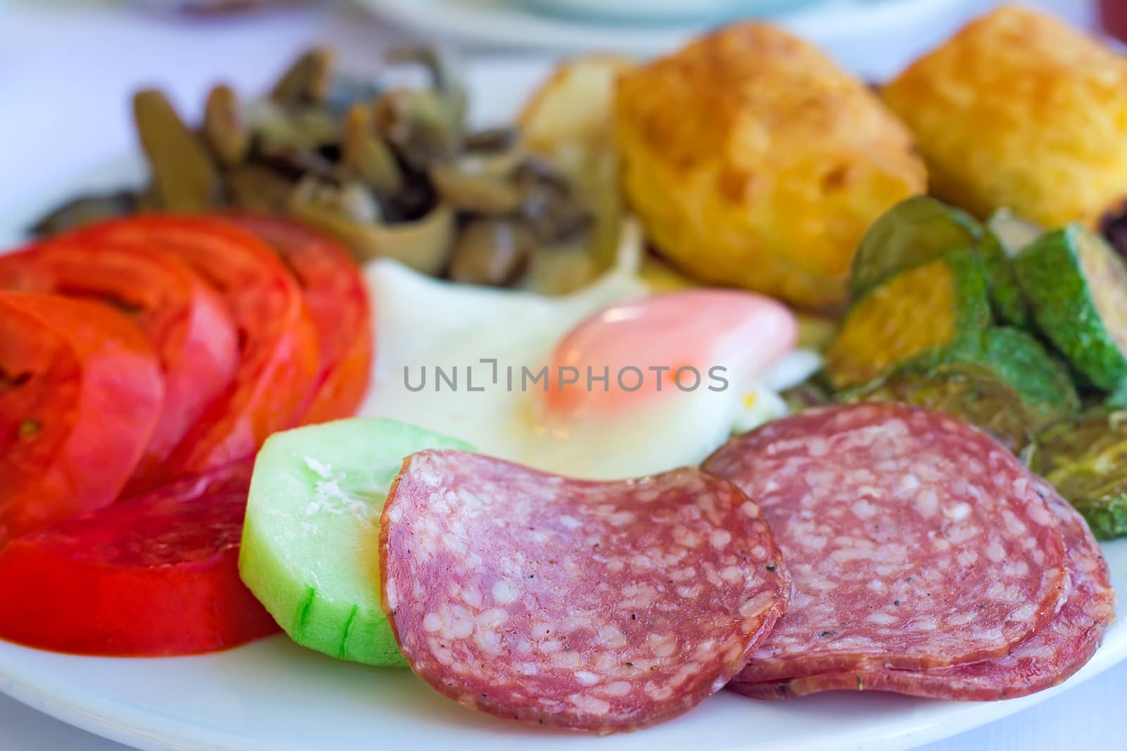 Sliced delicious slices of sausage and scrambled eggs with tomatoes and grilled zucchini on the plate on the table.