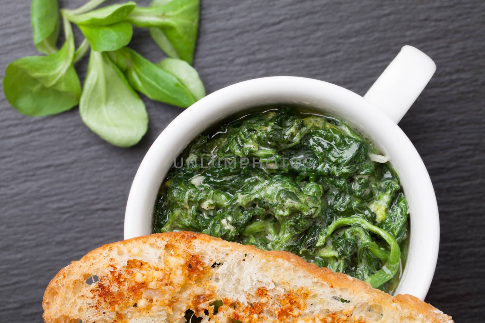 Appetizer sauteed garlic spinach dish in cup, baked bread slice  with  melted cheese served on black stone