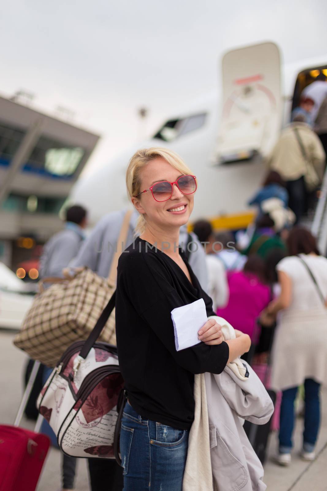 Cheerful woman holding carry on luggage queuing to board the commercial airplane.