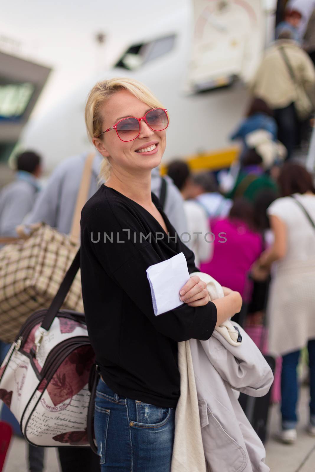 Joyful woman holding carry on luggage queuing to board the commercial airplane.