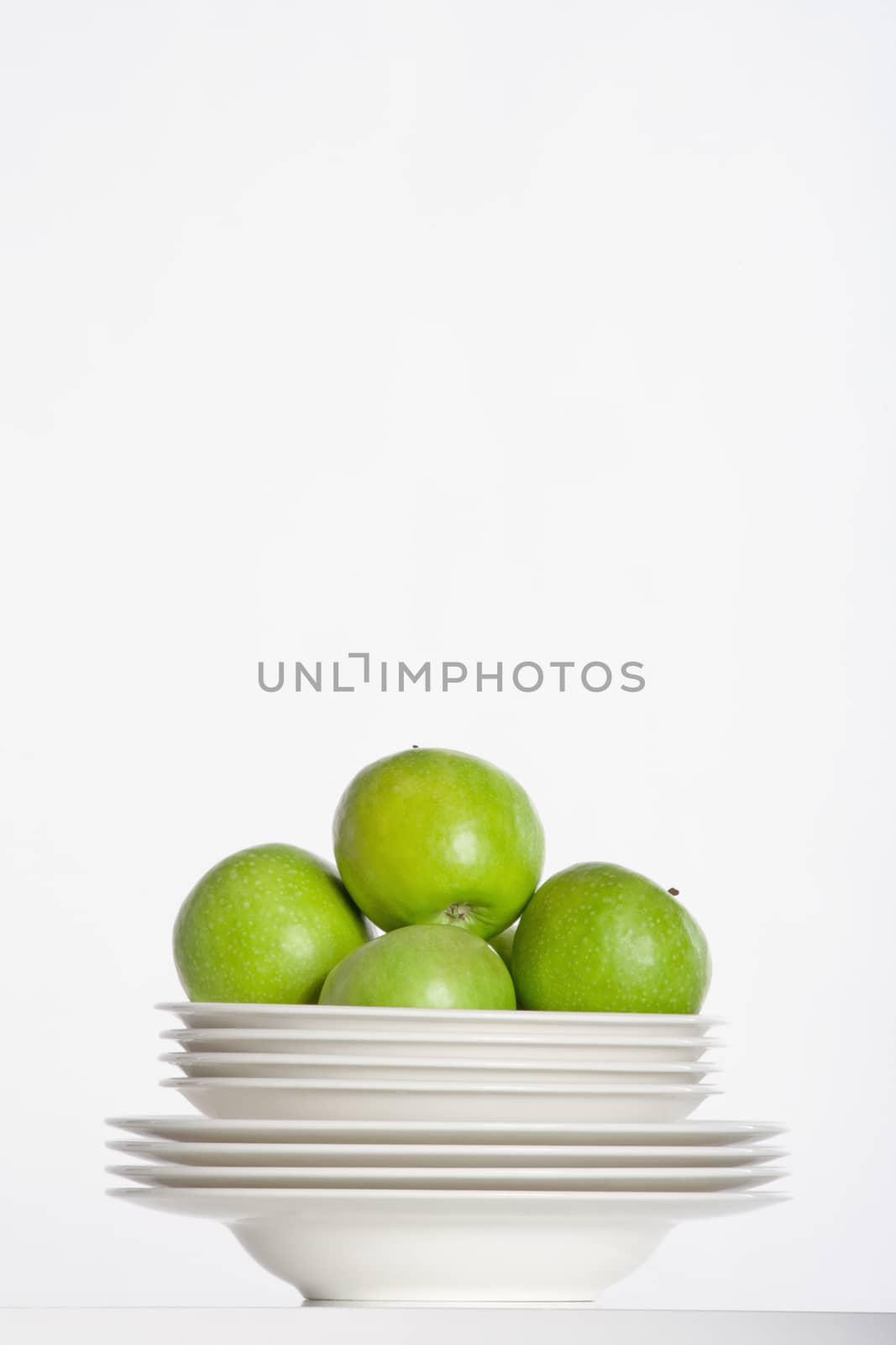 studio shot of a pile of plates and green apples isolated on white