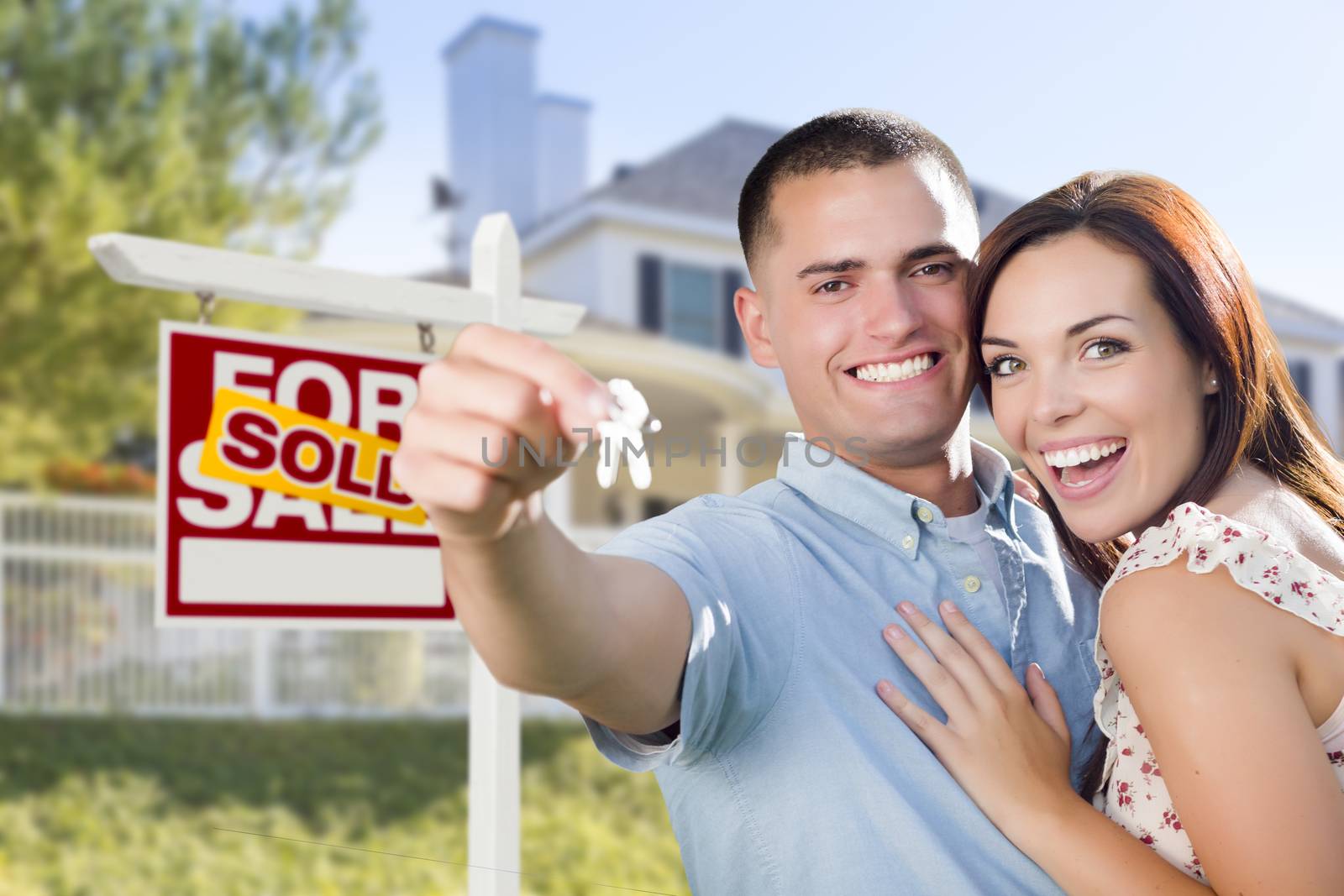 Mixed Race Excited Military Couple In Front of New Home with New House Keys and Sold Real Estate Sign Outside.