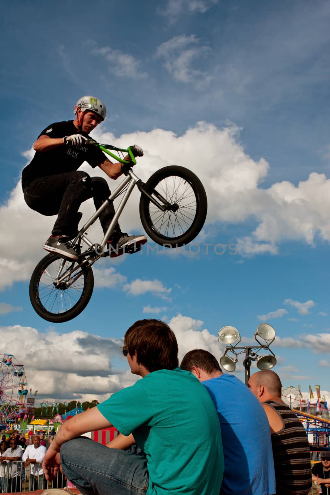 Hampton, GA, USA - September 27, 2014:  A young man with the High Roller BMX club performs a stunt jumping directly over three teen audience members sitting on the ramp, at the Georgia State Fair.