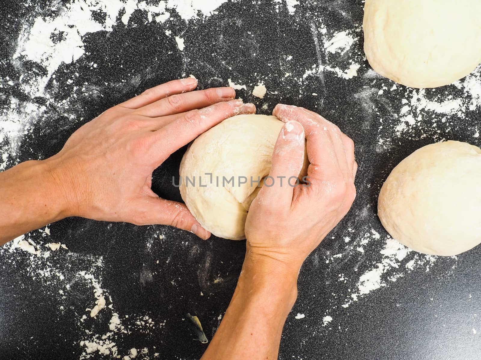 Hands kneading dough on black board with flour by Arvebettum
