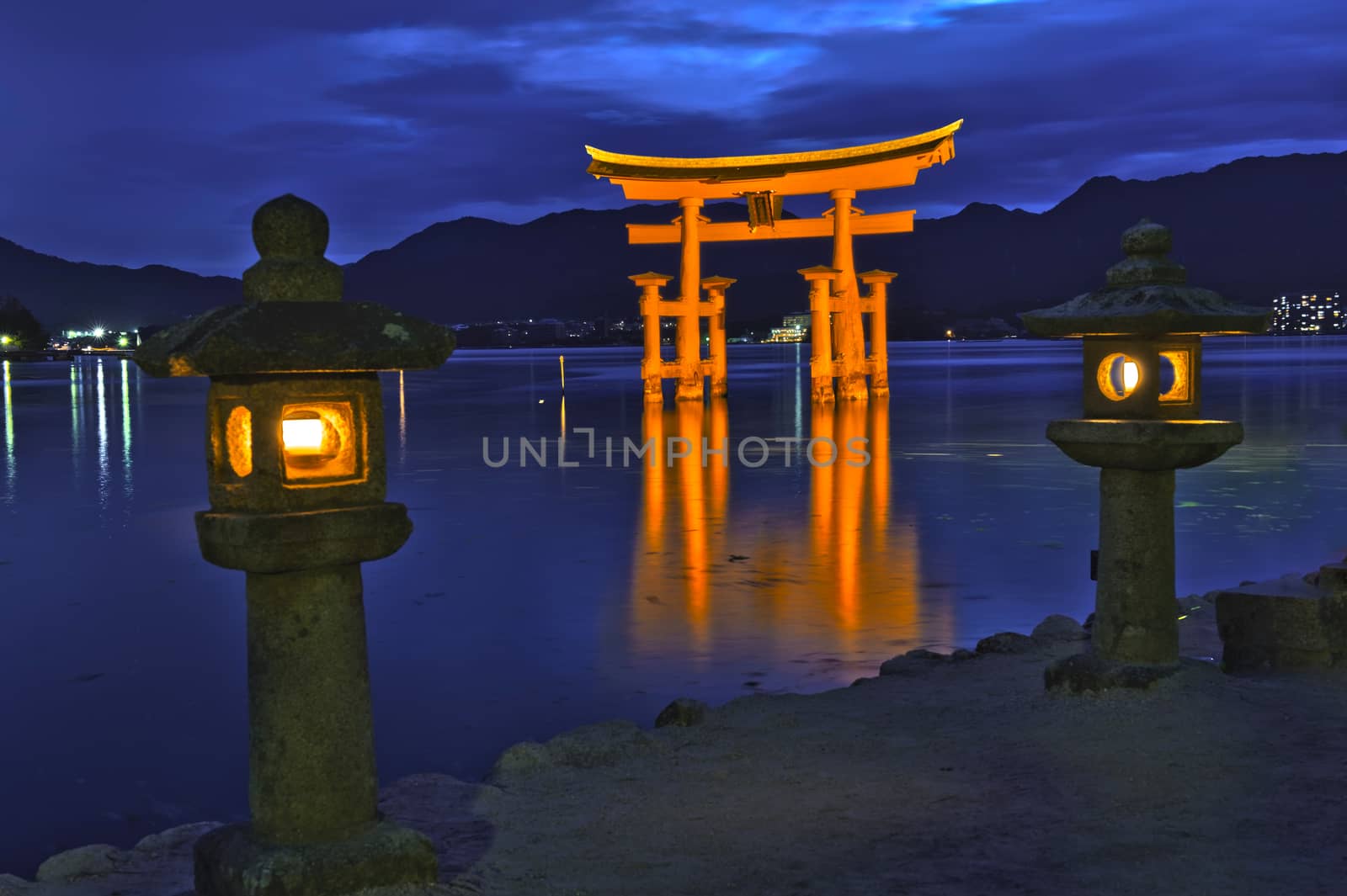 Great floating gate (O-Torii) on Miyajima island near Itsukushima shinto shrine, Japan shortly after the sunset with lit lanterns on the shore