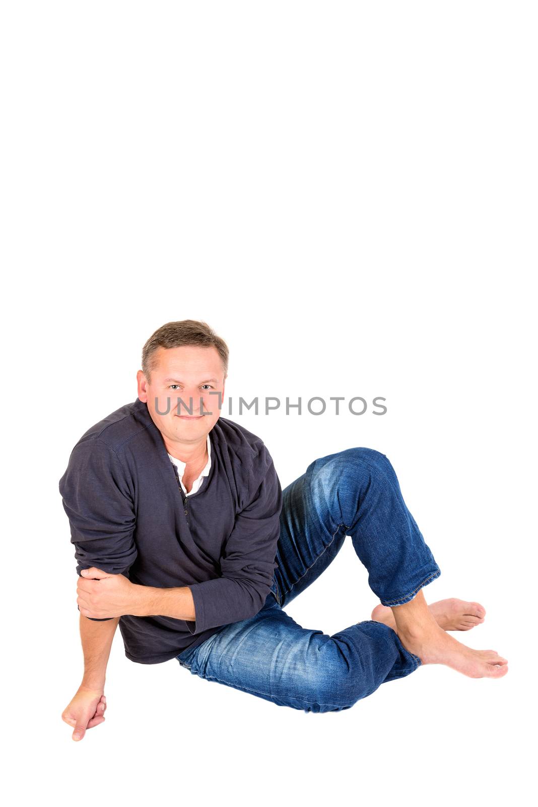 Casually dressed middle aged man smiling. Sitting on a floor barefoot man shot in vertical format isolated on white.