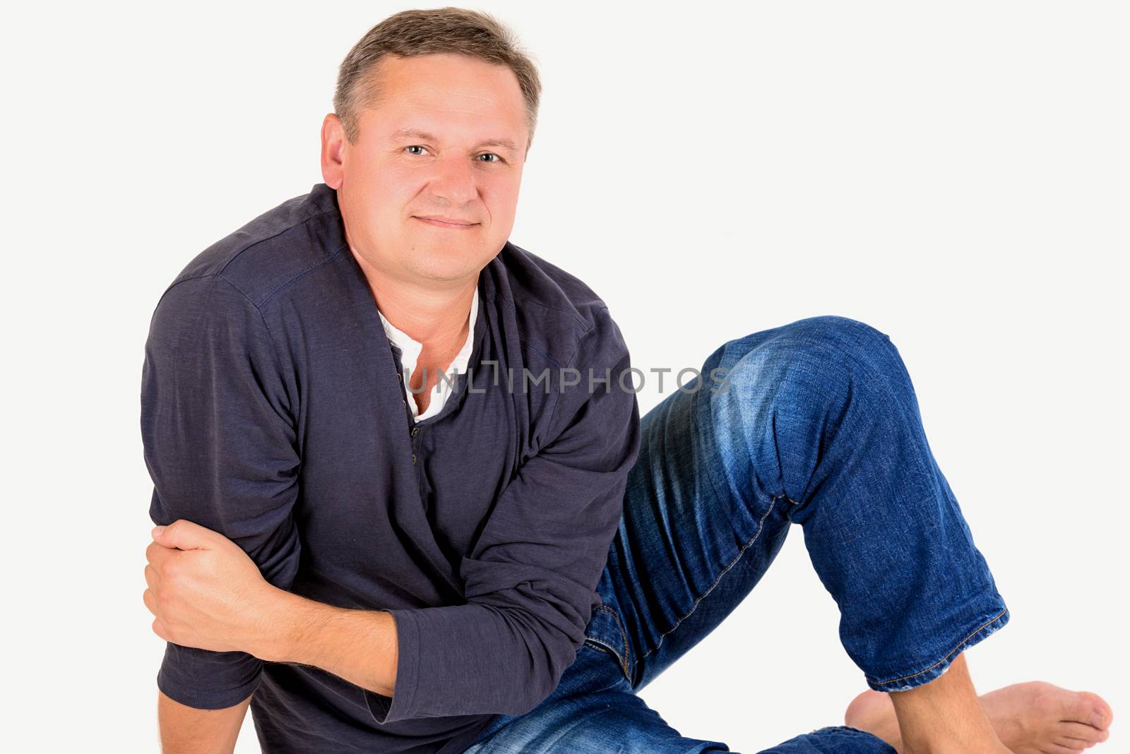 Casually dressed middle aged man barefoot sitting on a floor. Man shot in horizontal format isolated on white.