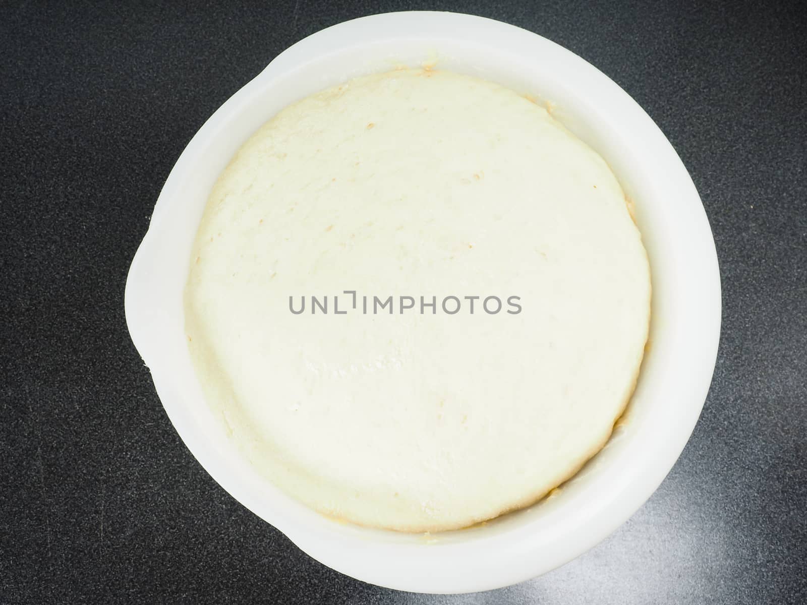 Proven dough in a white plastic bowl on black table by Arvebettum