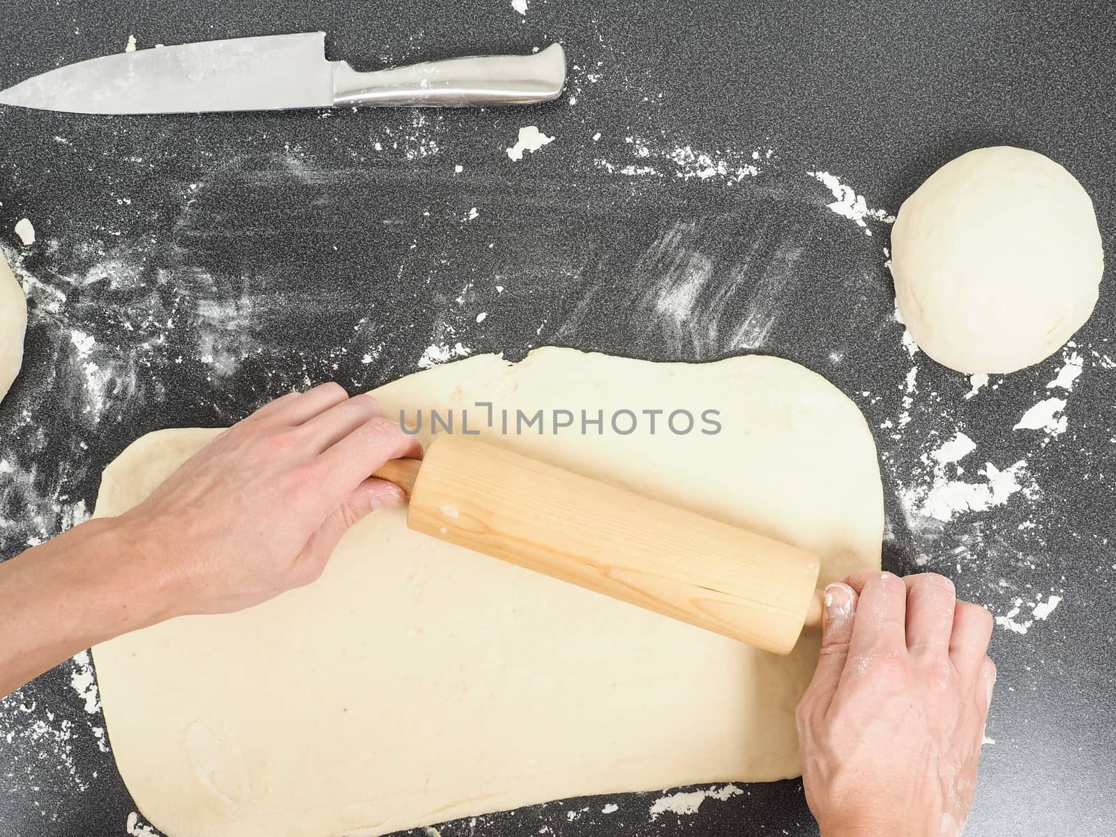 Person handling a dough with a rolling pin floured black table  by Arvebettum