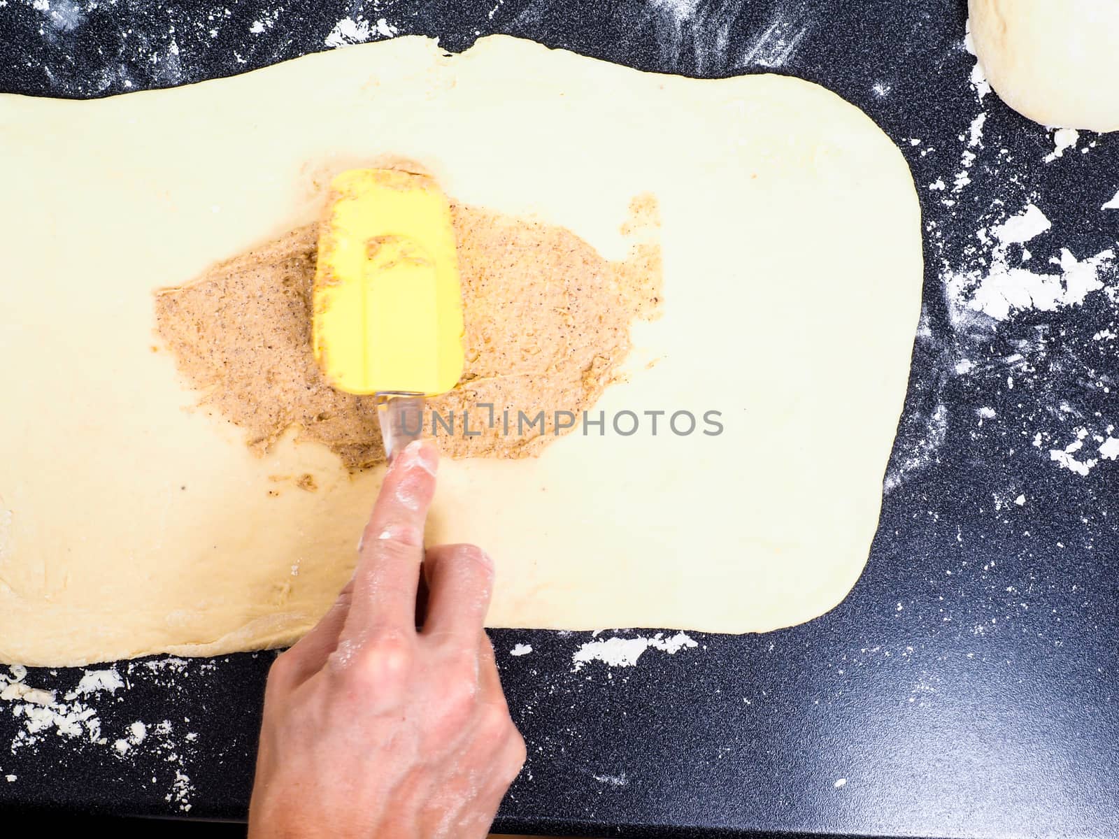 Person spreading cinnamon mix with spatula onto a flattened dough before rolling