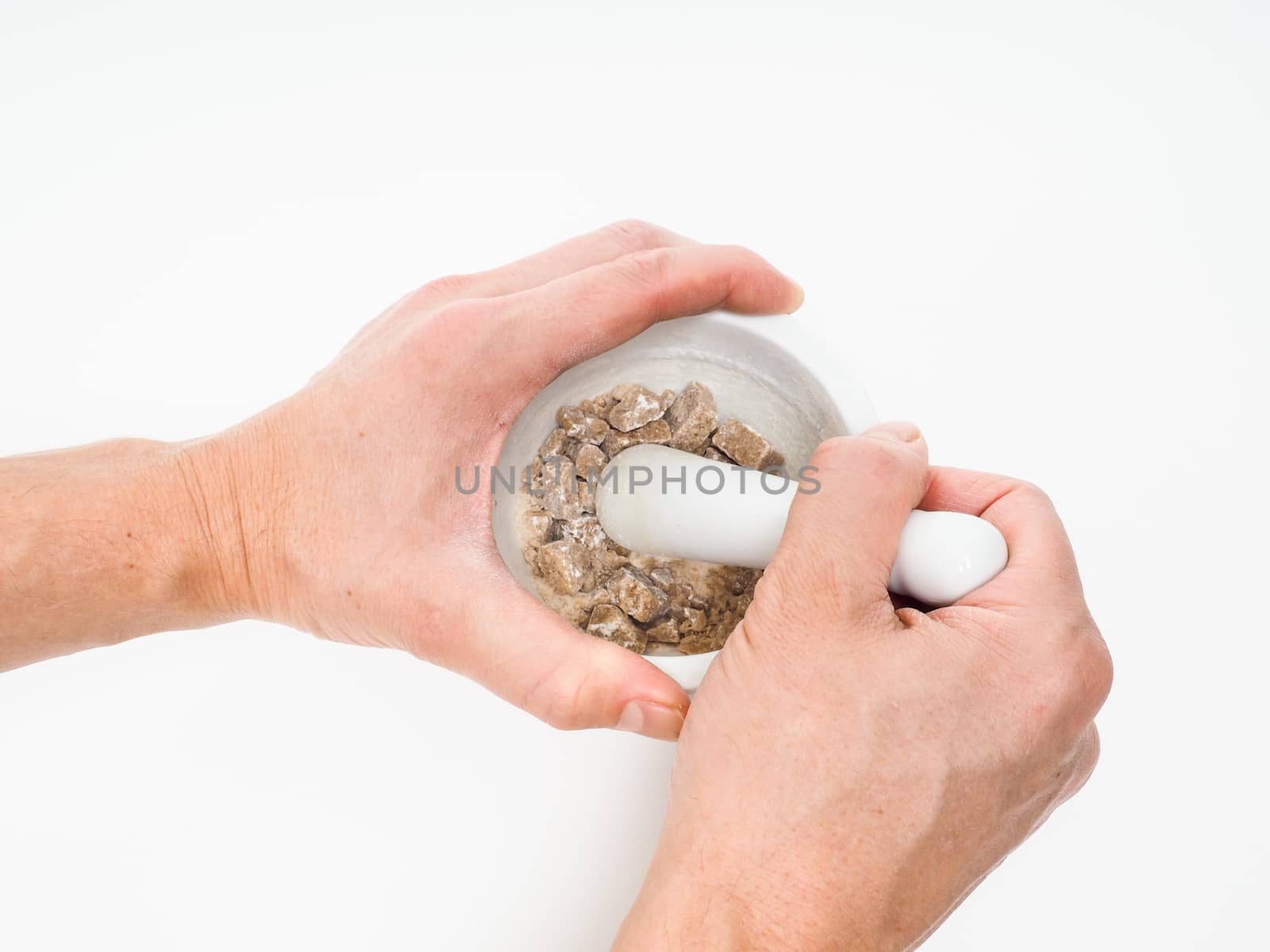 Person crushing brown sugar cubes in a white marble mortar by Arvebettum