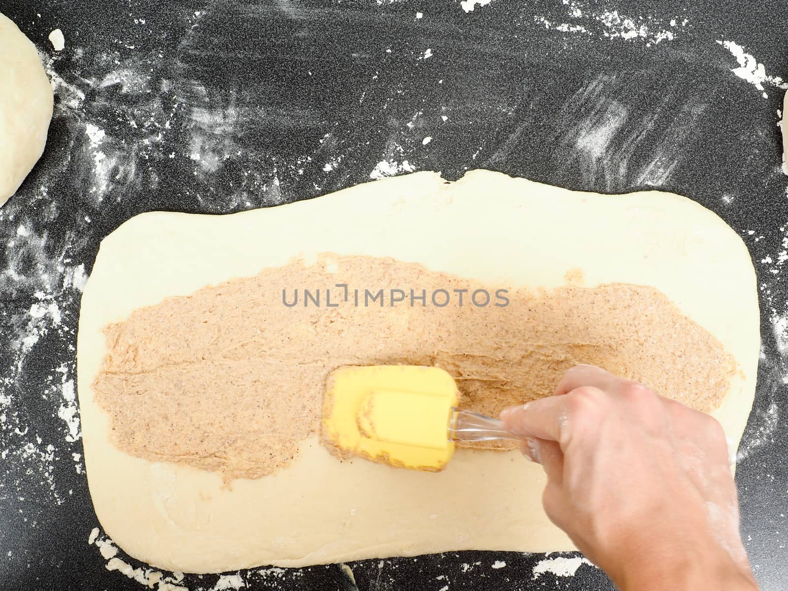 Person spreading cinnamon mix with spatula onto a flattened doug by Arvebettum