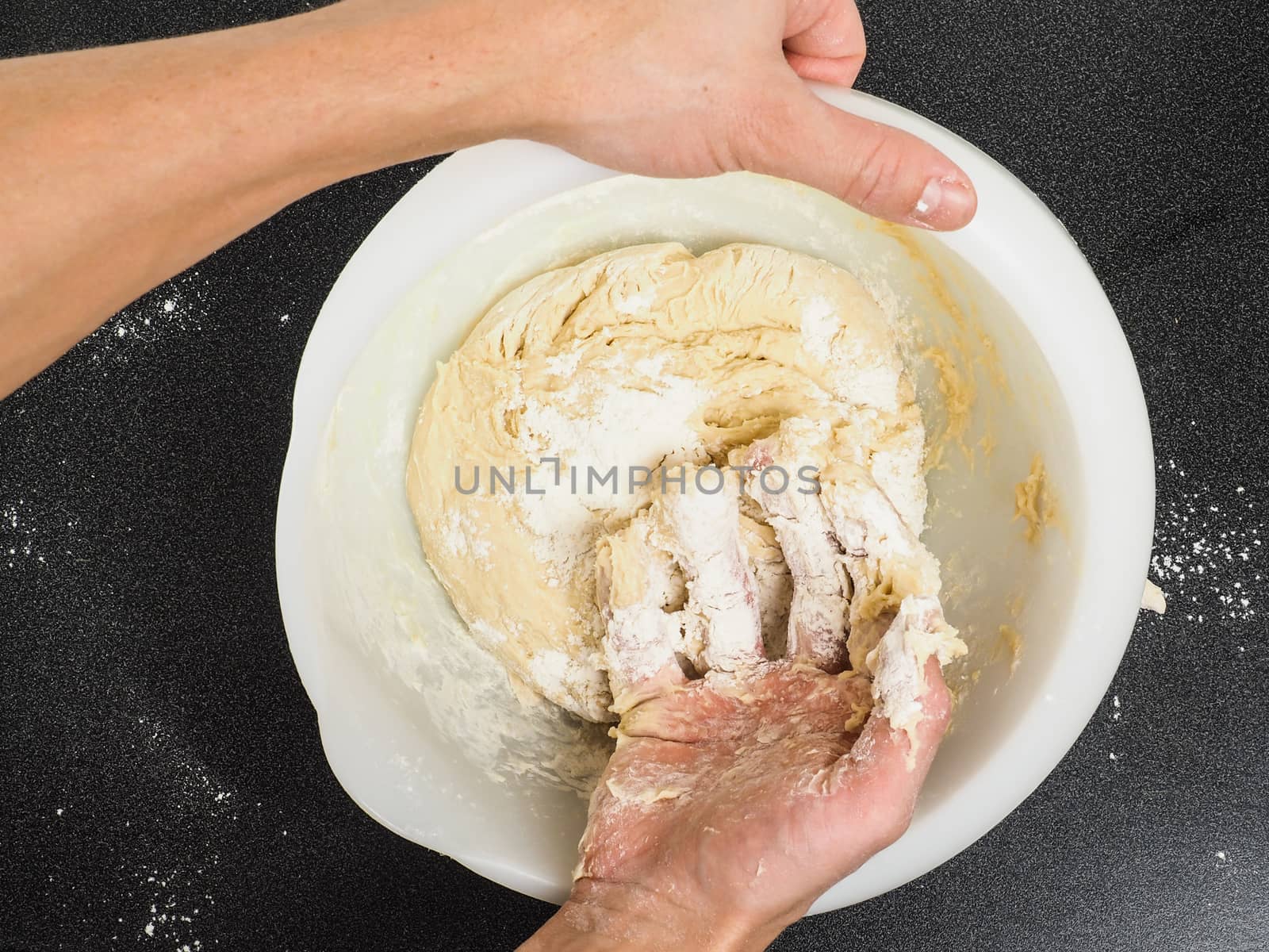 Person kneading a sticky dough in white bowl on black table