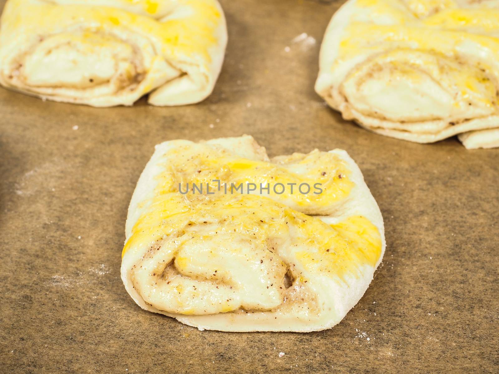 Plaited cinnamon rolls on baking paper with egg wash by Arvebettum
