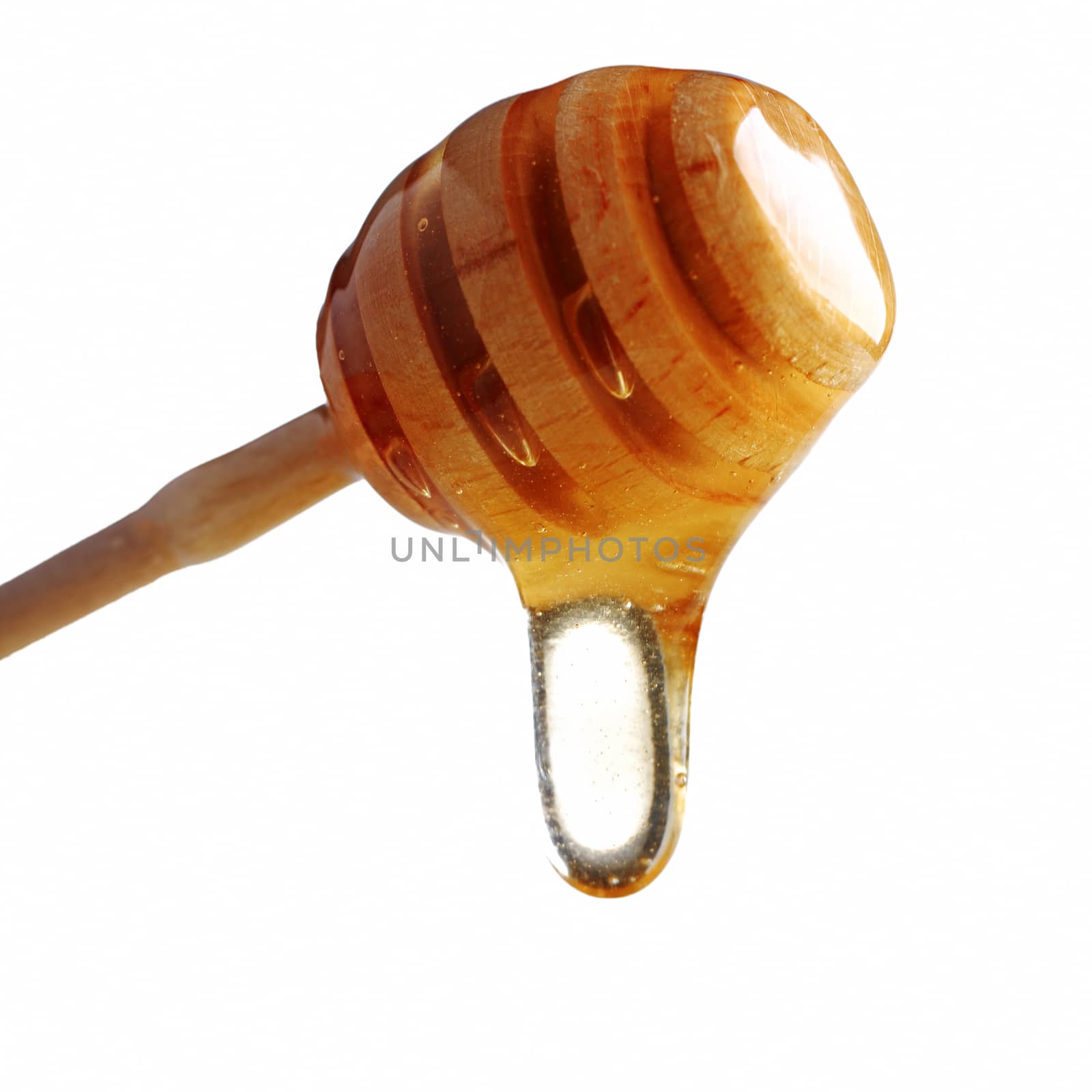 Honey dripping from a wooden honey dipper isolated on white background