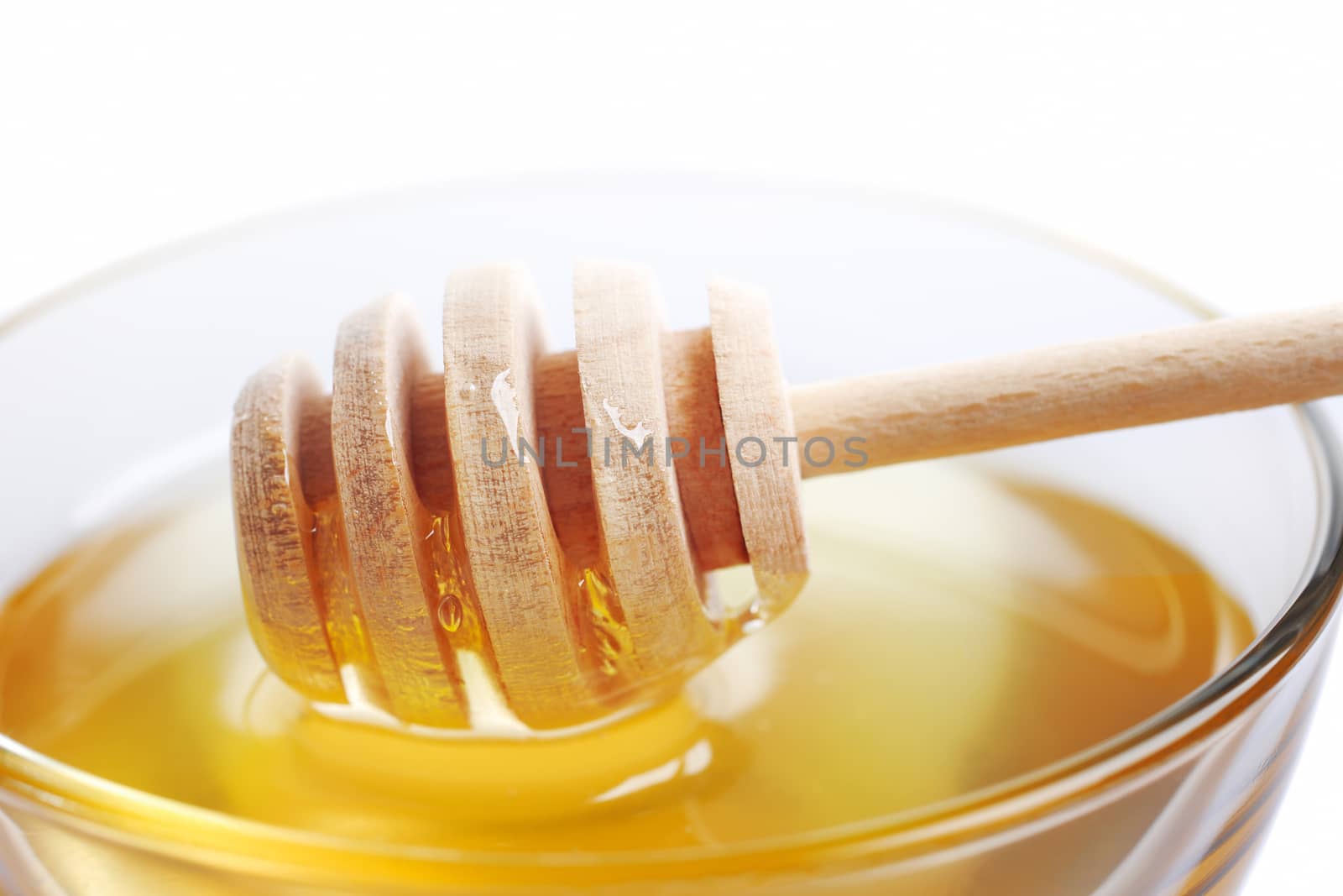 Glass bowl with floral honey and stick isolated on white background.