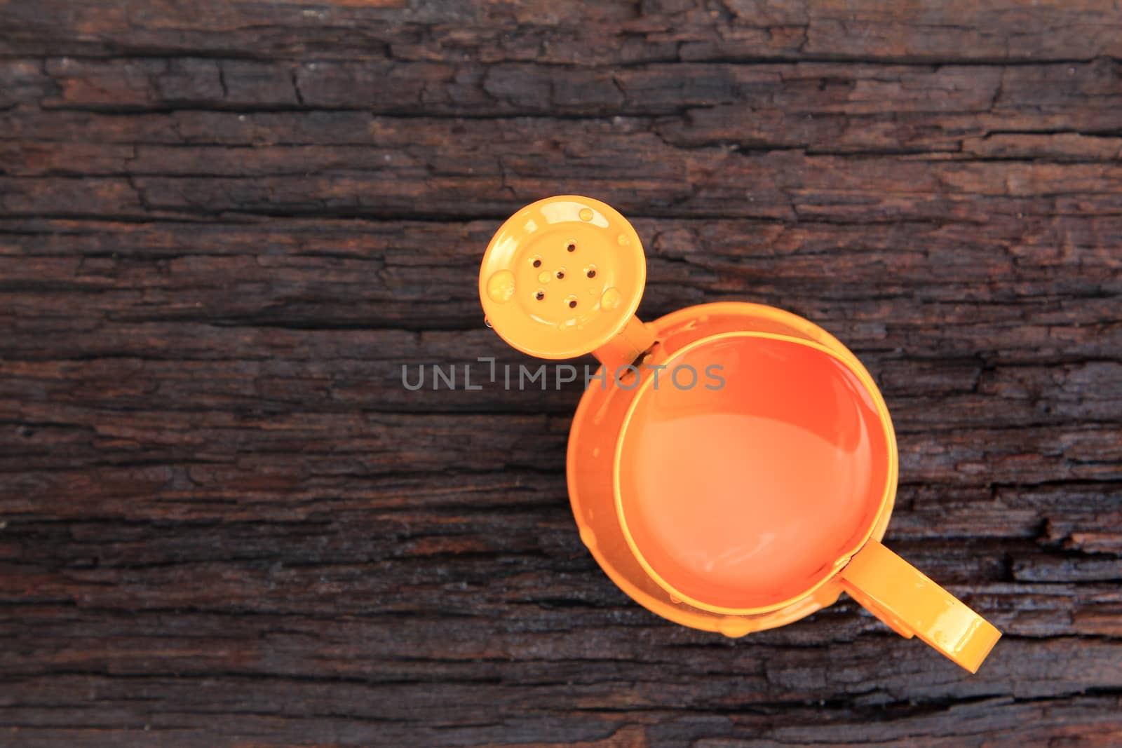 Orange watering can on old wood background