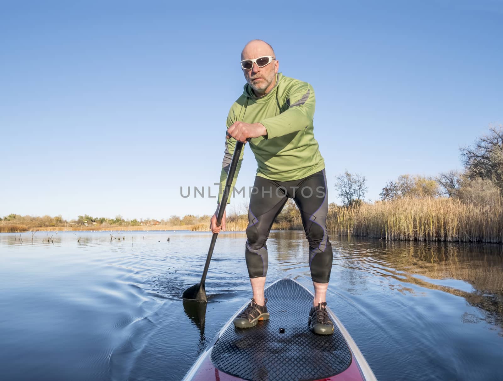 senior paddler in life jacket enjoying stand up paddling on lake, fall scenery in Fort Collins, Colorado