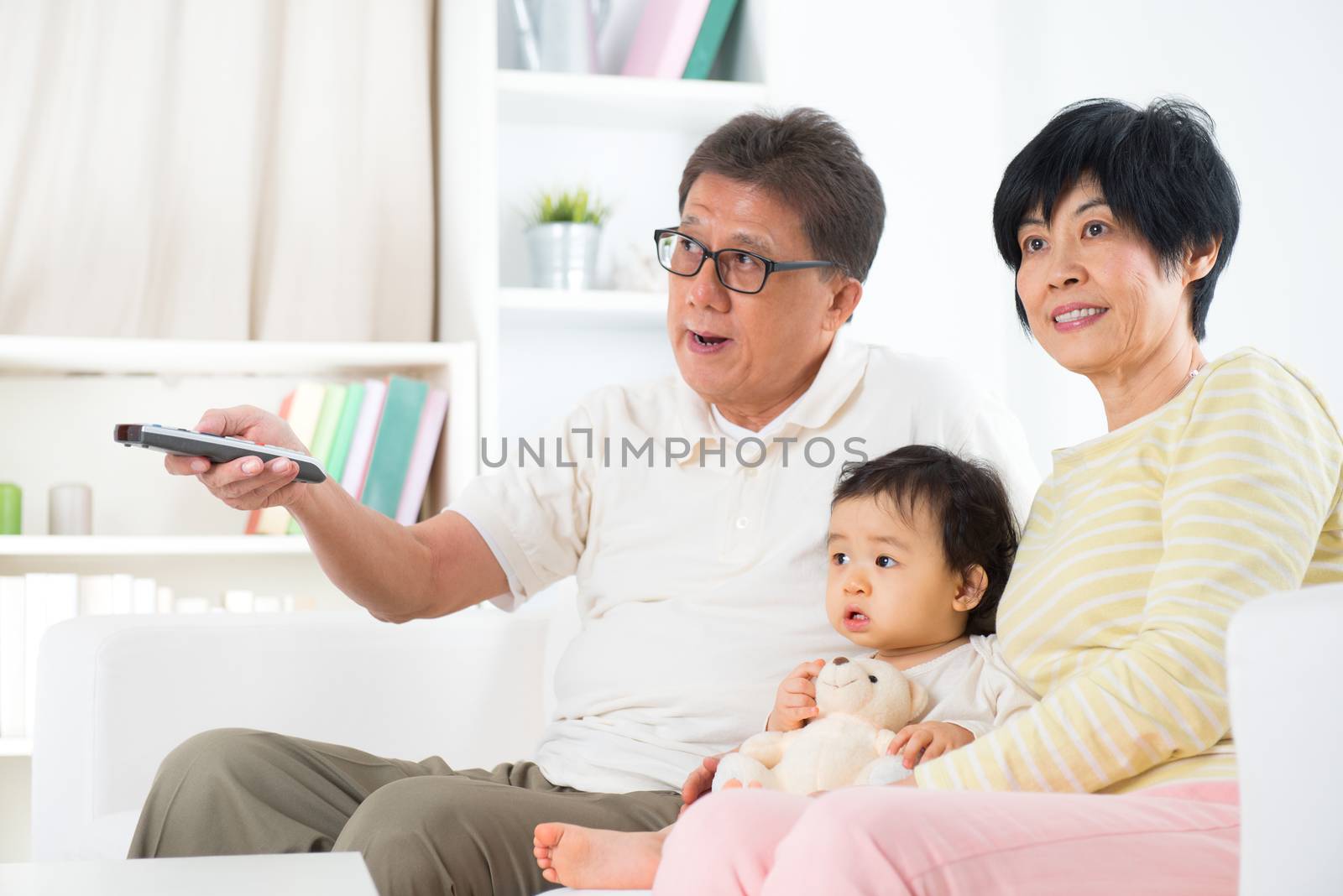 Asian family watching movie together, grandparents and grandchild indoor living lifestyle at home.