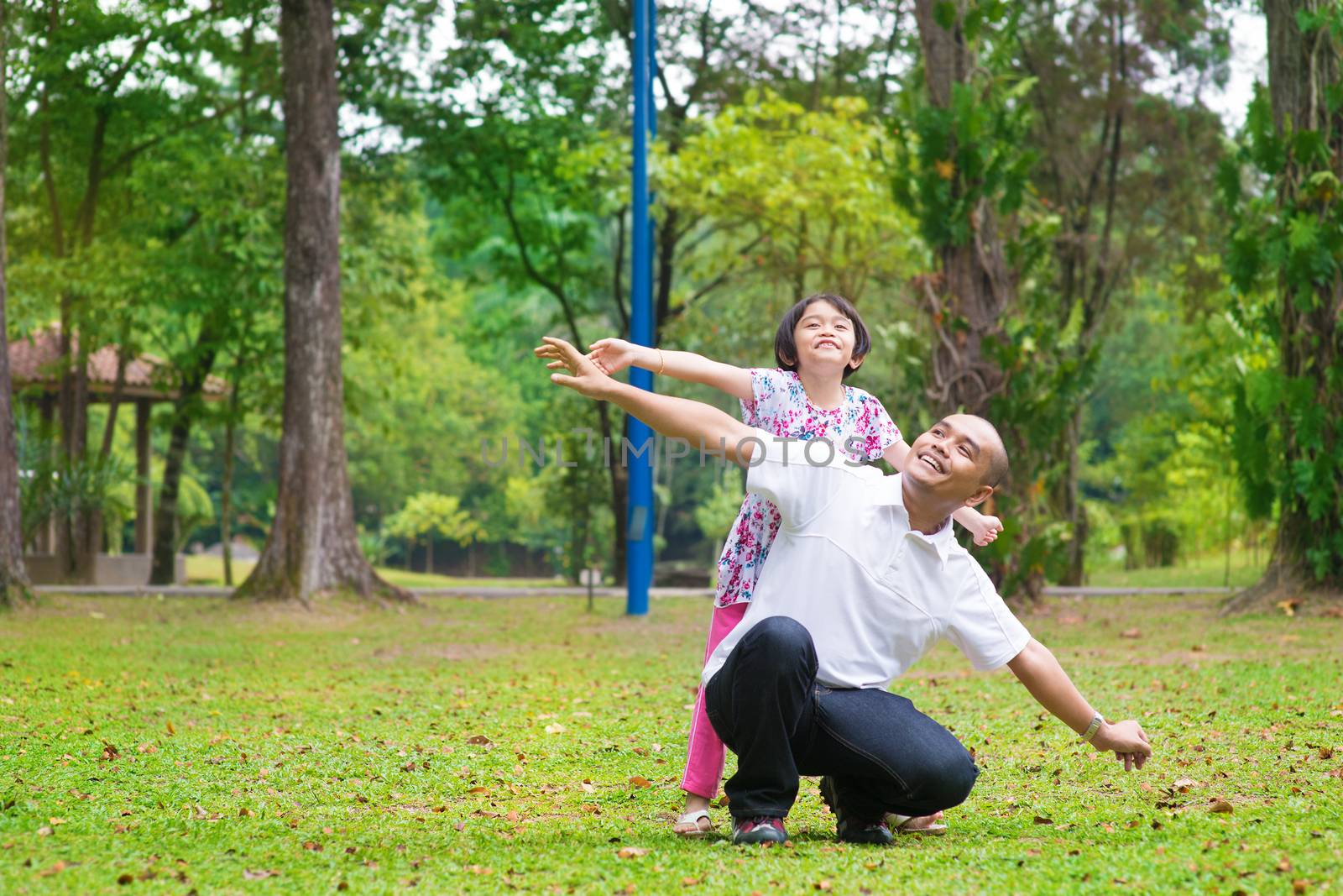 Father and daughter playing at outdoor garden park. Happy Southeast Asian family living lifestyle.
