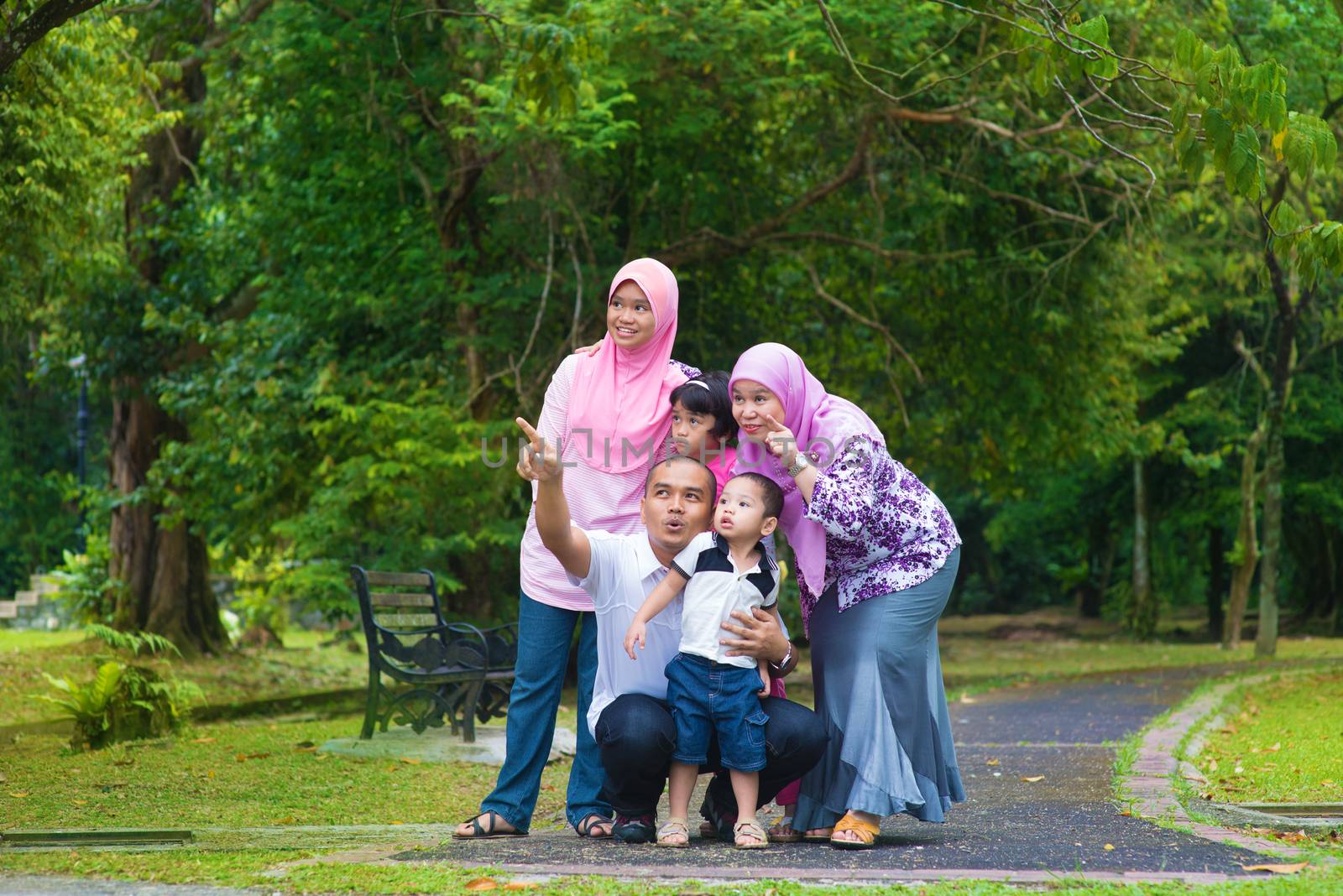Happy Southeast Asian family outdoor lifestyle at nature green park, pointing and looking away.