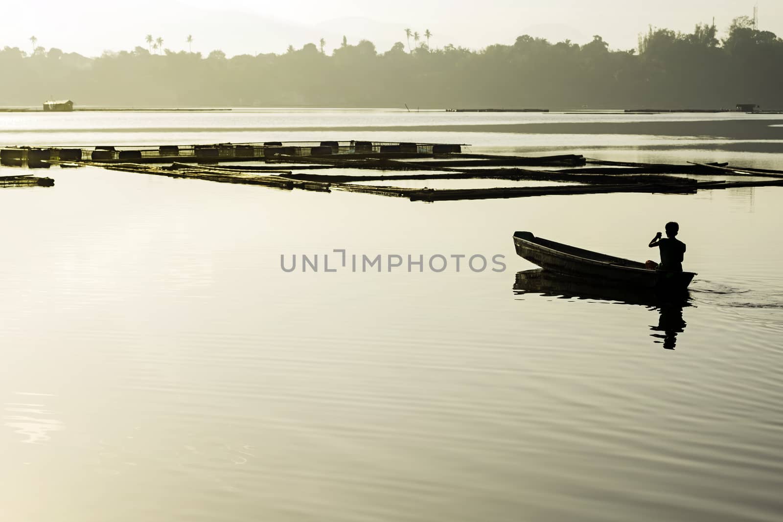 Man paddles towards his lake fishpens at sunrise
